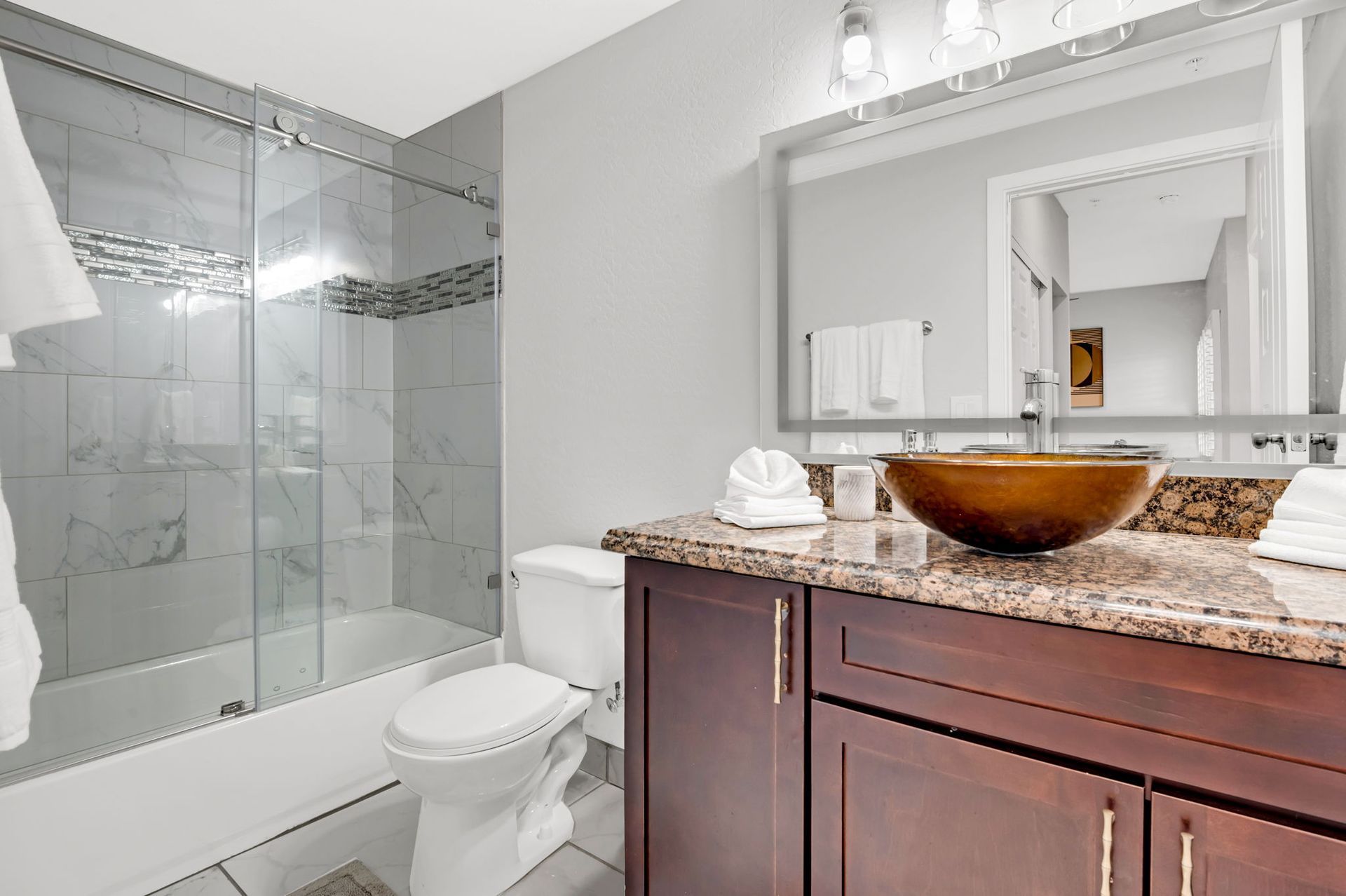 Bathroom with a brown vanity, a toilet, a shower/tub, and a large mirror.