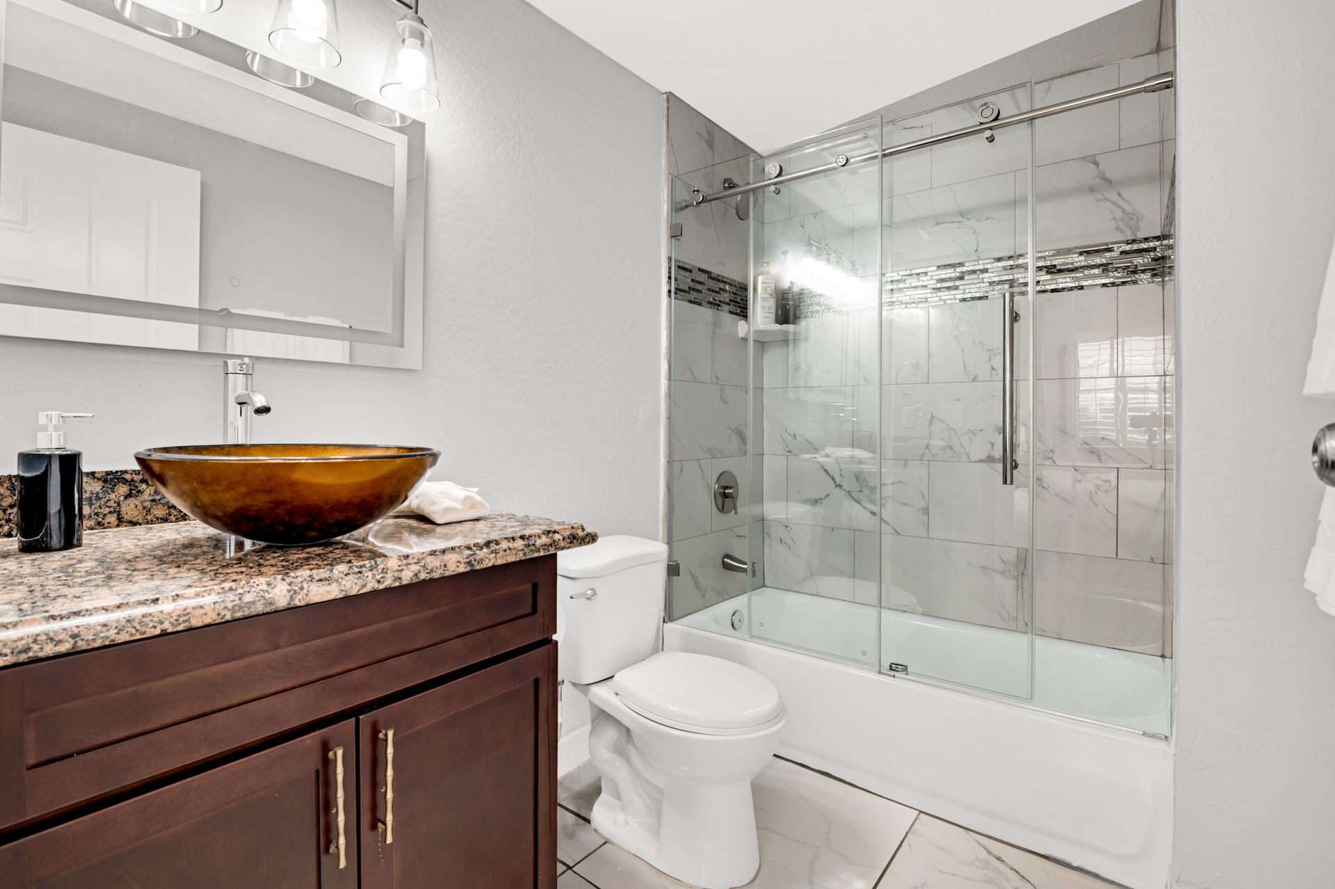 Bathroom with brown vanity, vessel sink, and glass shower enclosure. Gray walls and white fixtures.