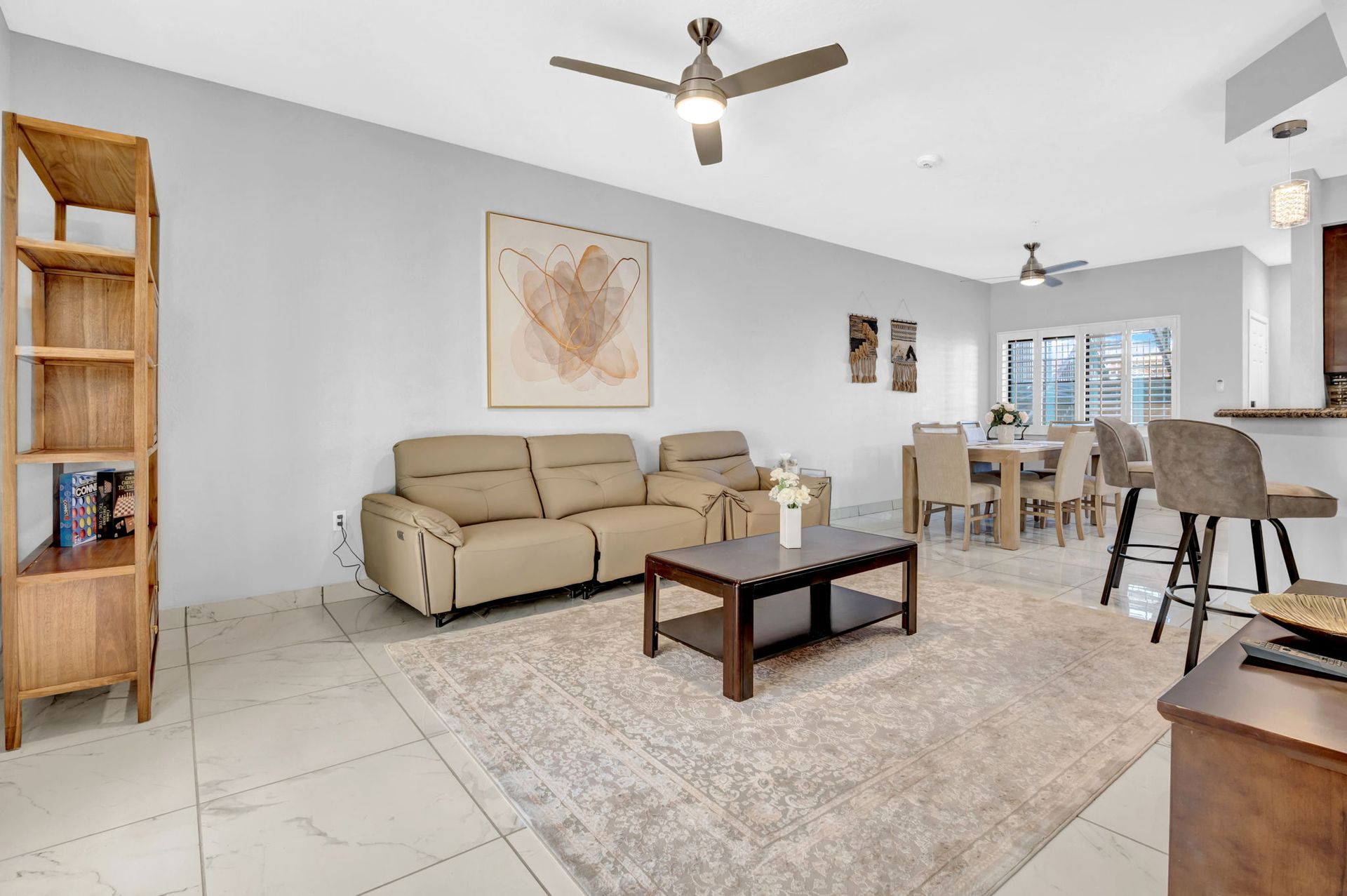 Open-concept living room with light-colored walls, furniture, and flooring. Contains a sofa, coffee table, and dining area.
