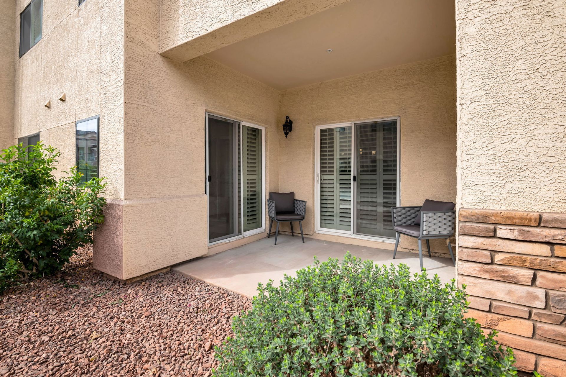 Patio with sliding doors, two chairs, and landscaping.