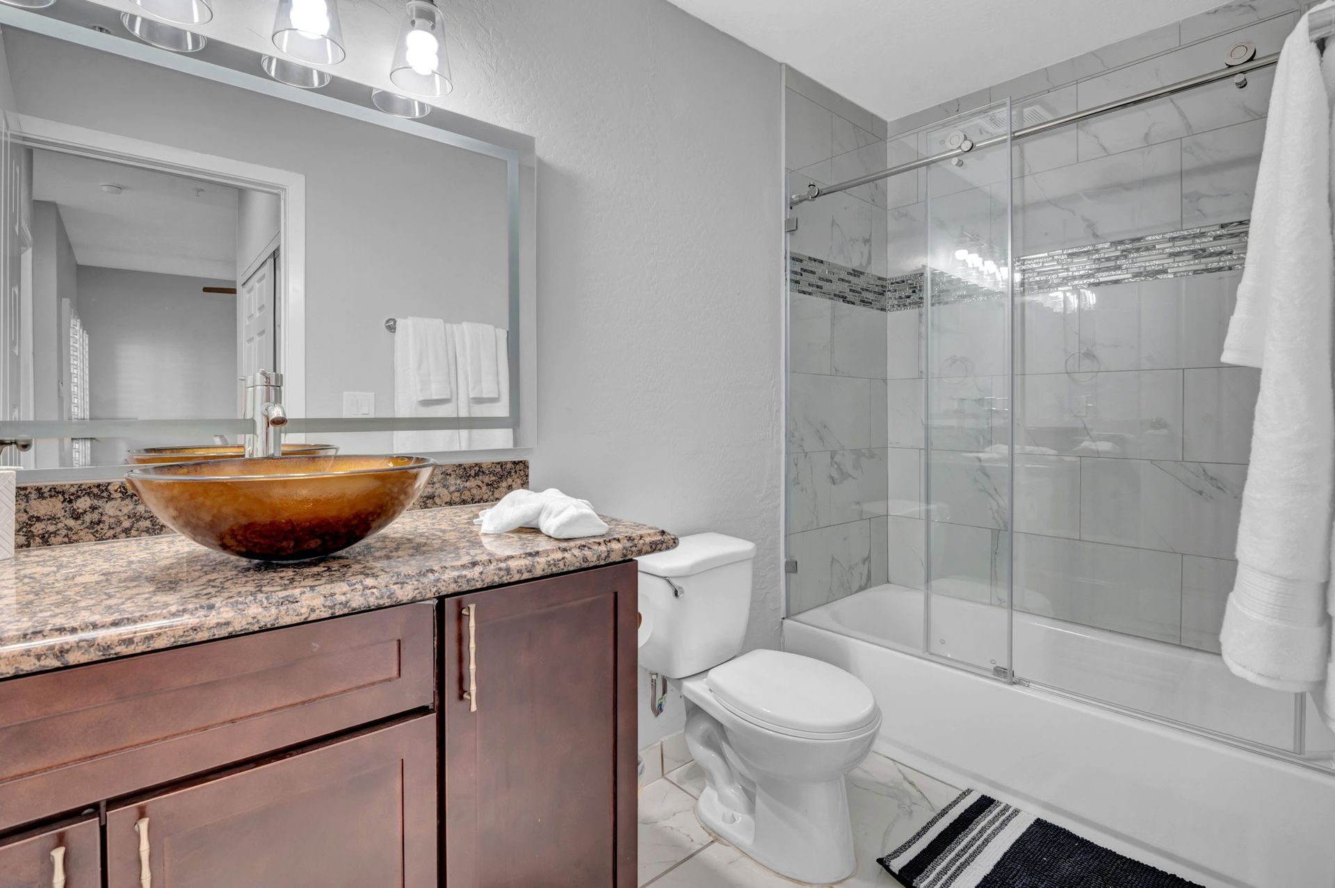 Bathroom with a granite countertop, brown sink, toilet, shower, and a towel hanging.
