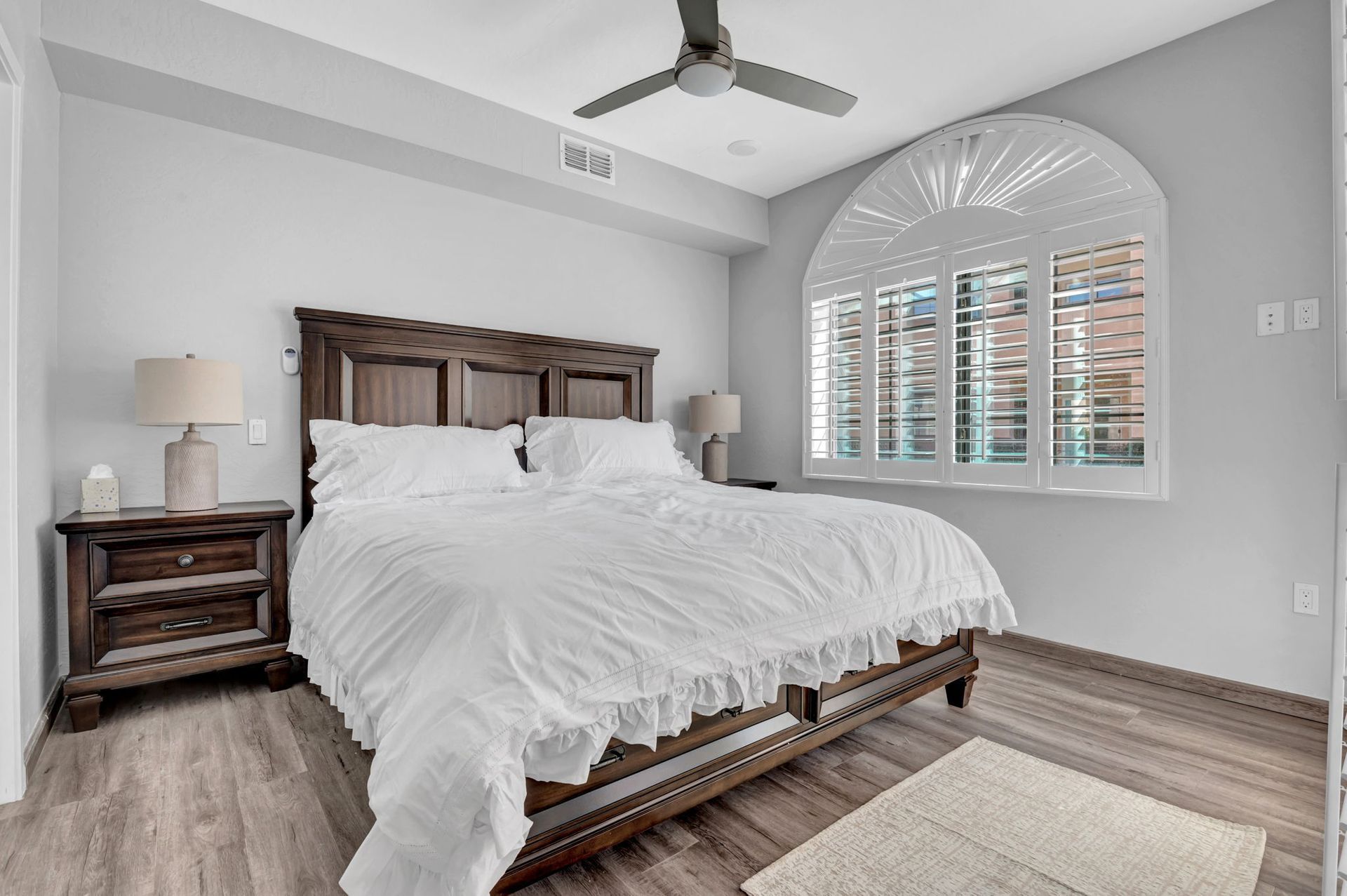 Bedroom with bed, nightstands, arched window, and ceiling fan.