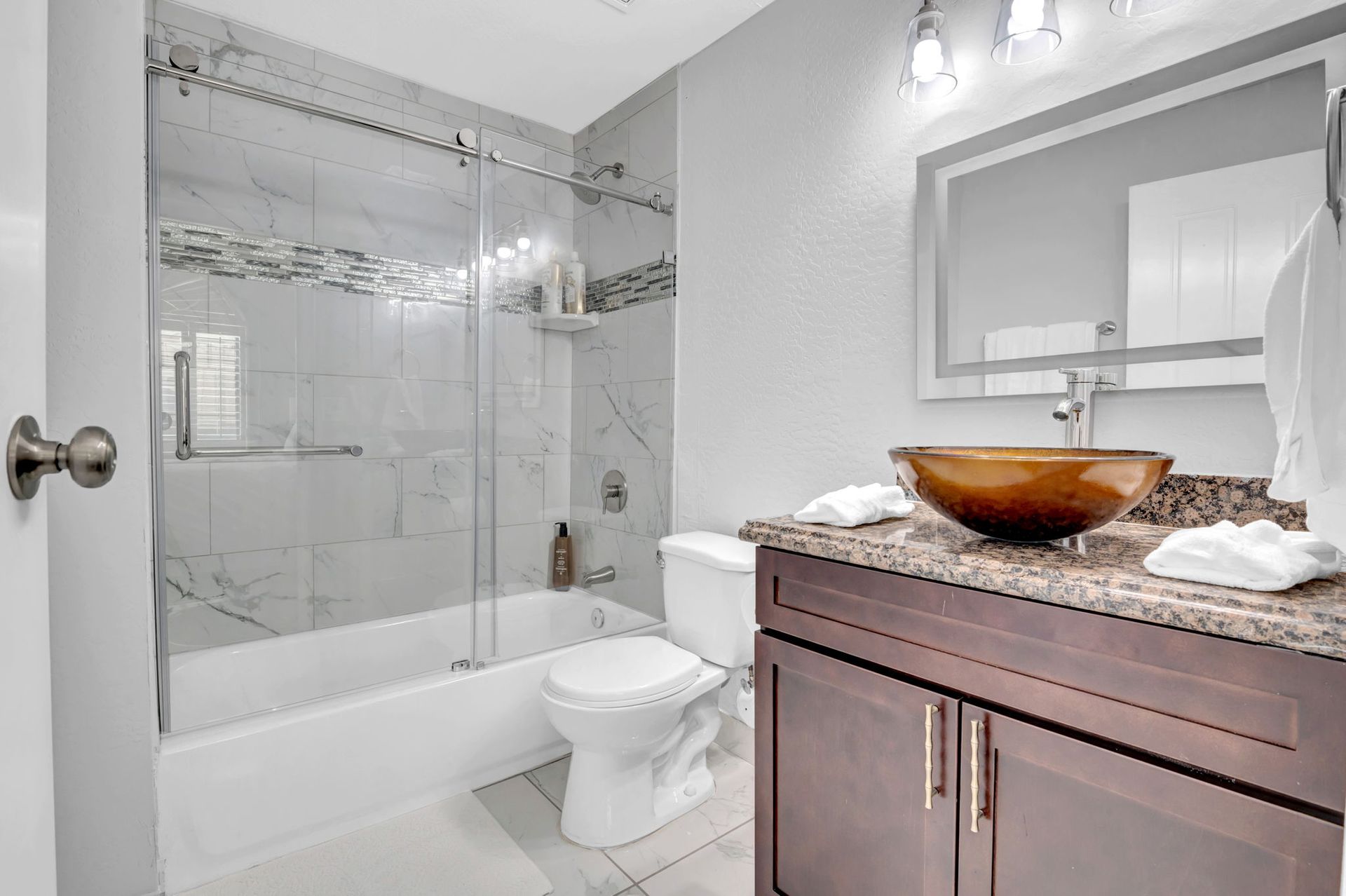 Bathroom with a glass shower, toilet, dark vanity with a brown vessel sink, and a framed mirror.