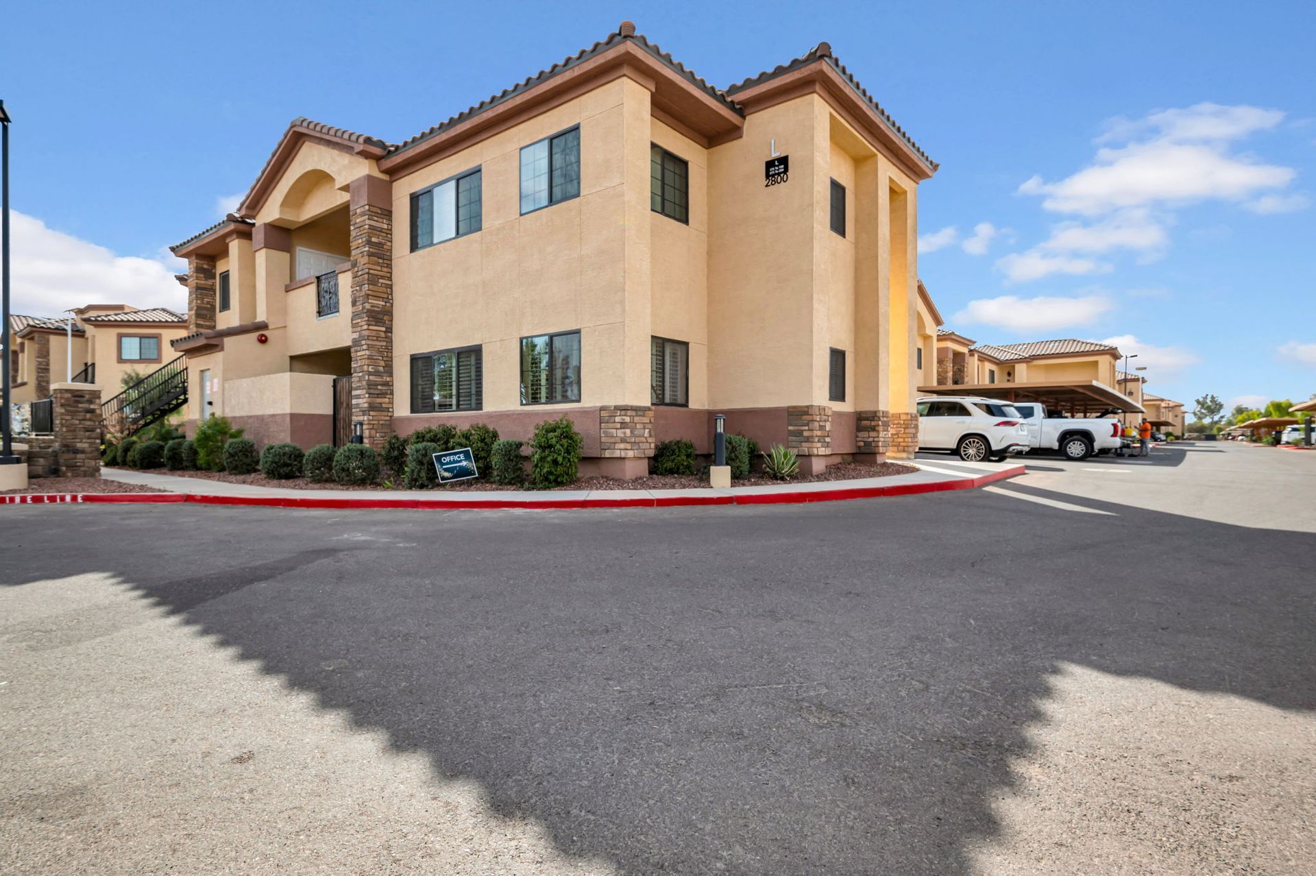 Apartment building with tan exterior, parking area, and blue sky.