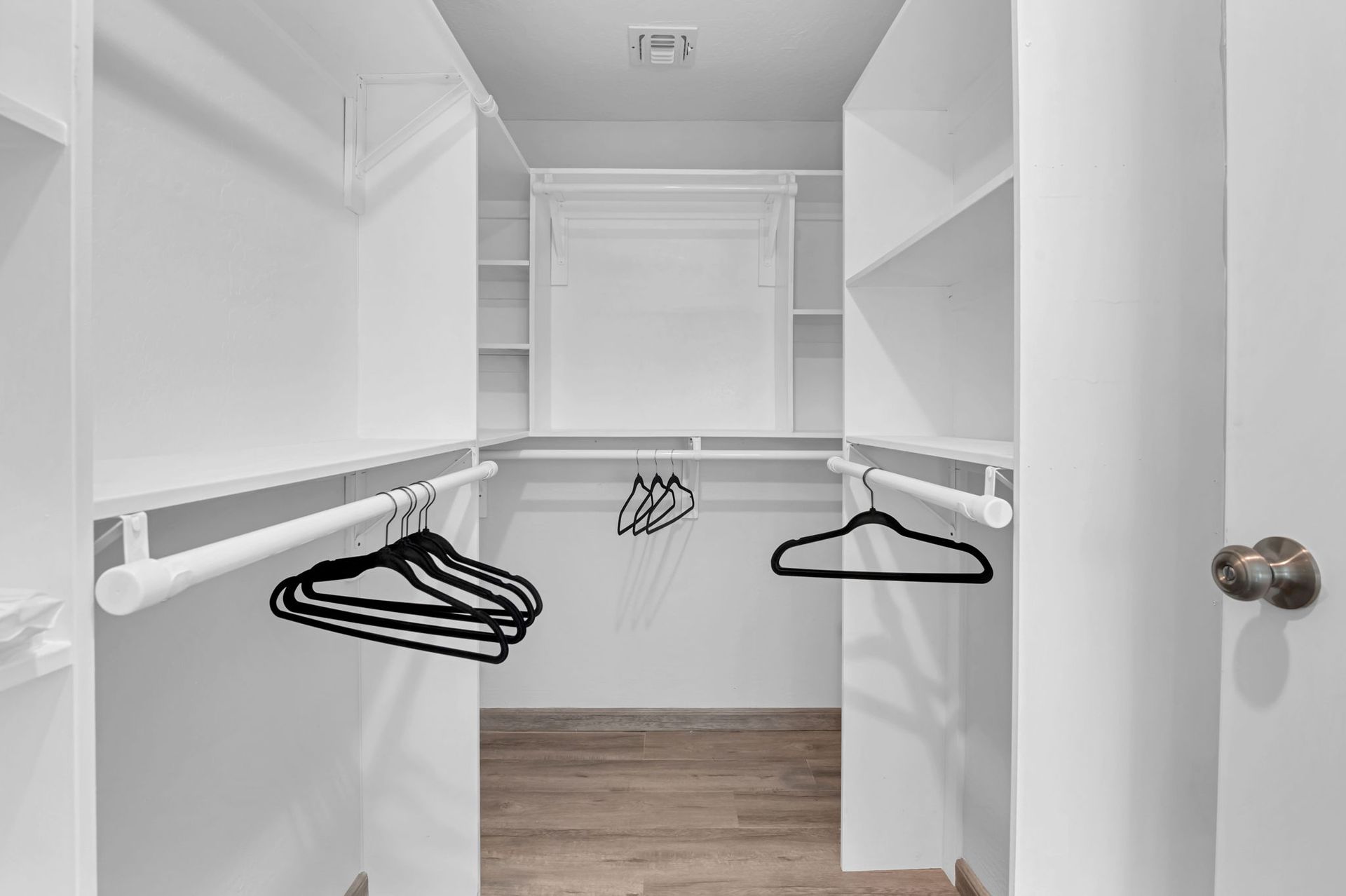 Walk-in closet with white shelves and rods; clothes hangers are visible.