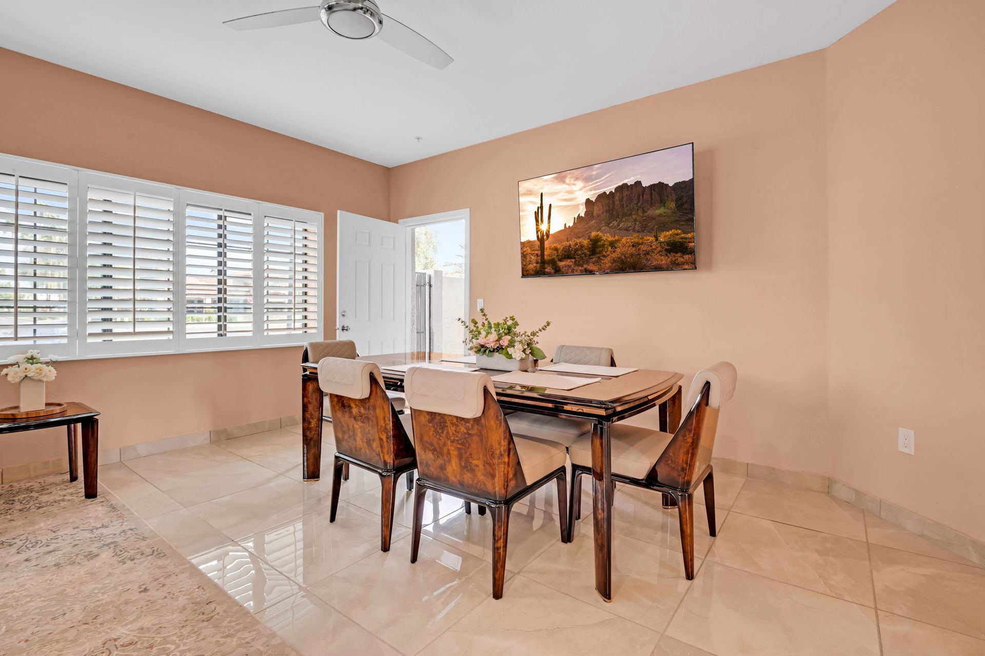 Dining room with table, chairs, art, shutters, and light pink walls.