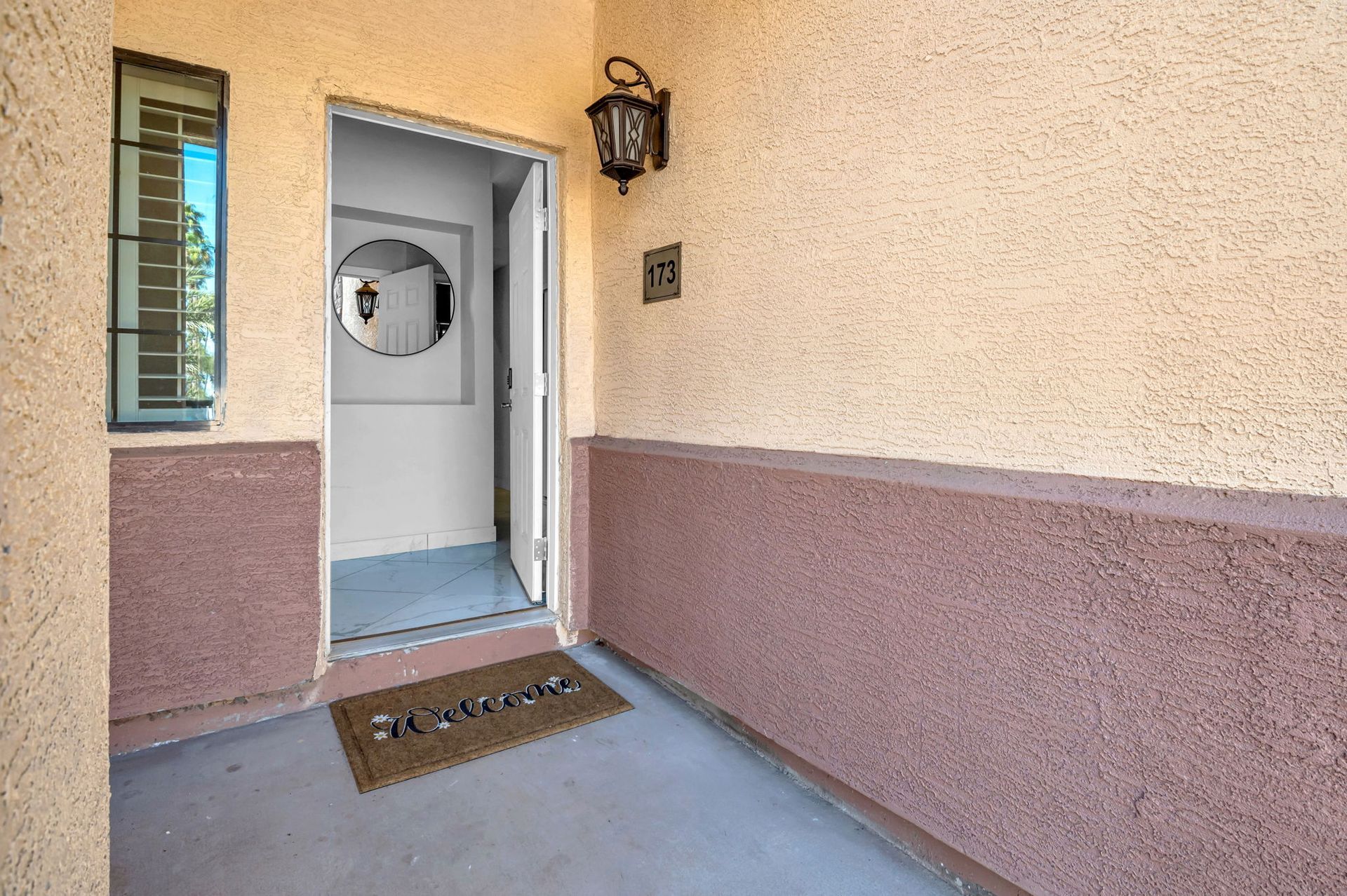 Exterior doorway with welcome mat, window, and wall-mounted light fixture.
