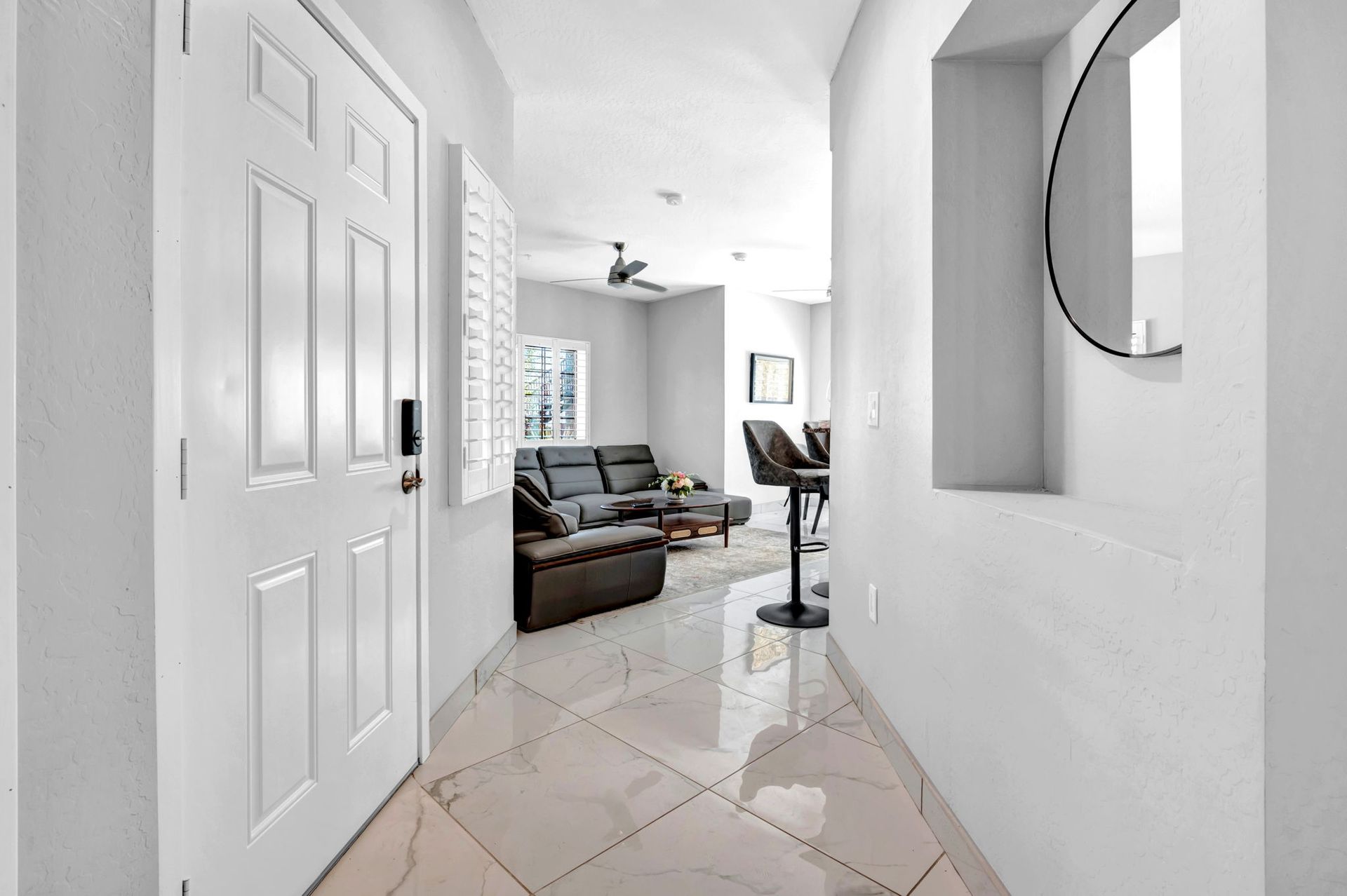 Hallway with white walls, a white door, and a glimpse of a living room with a sofa.