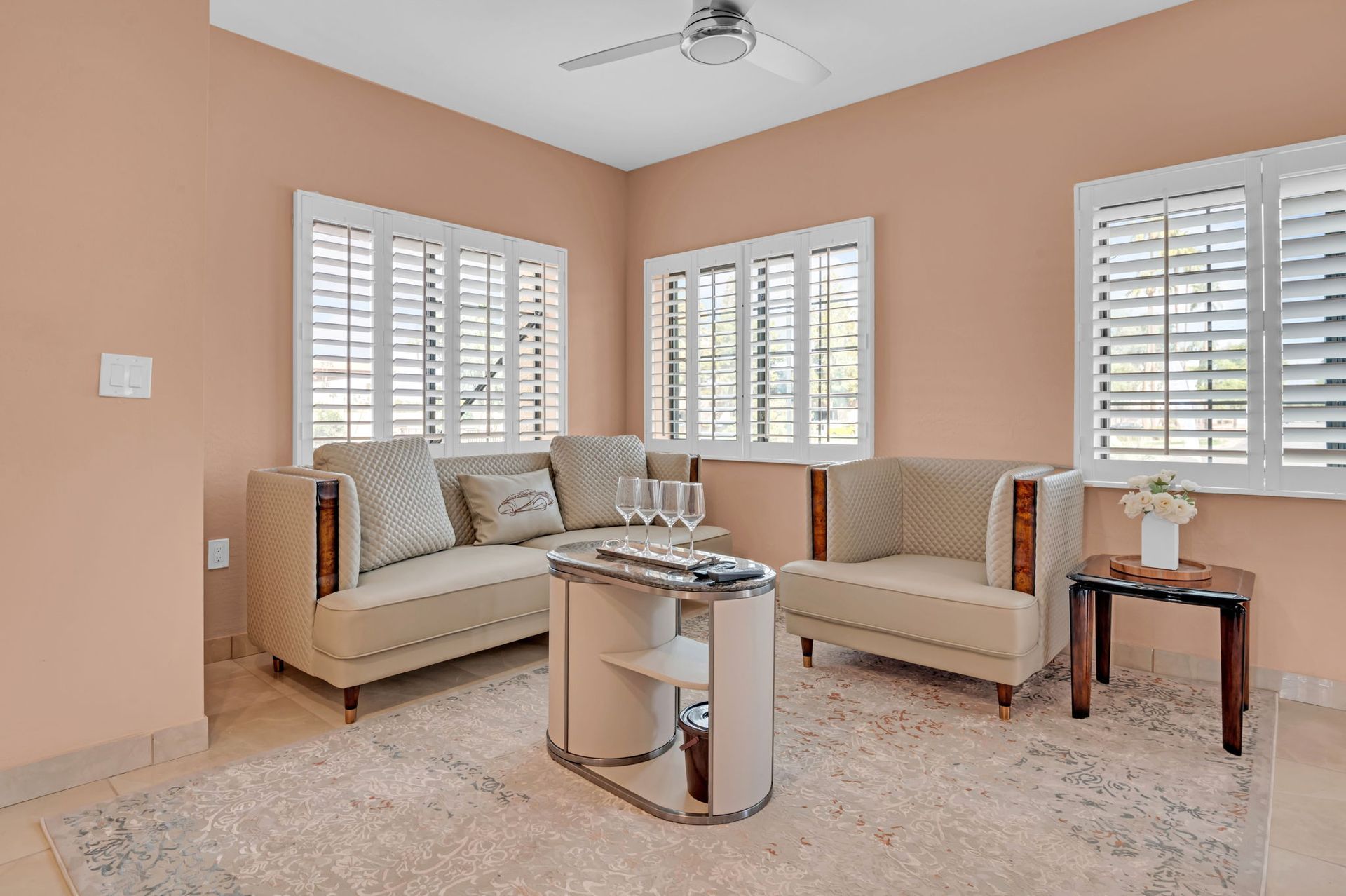 Living room with peach walls, white shutters, and cream-colored furniture.