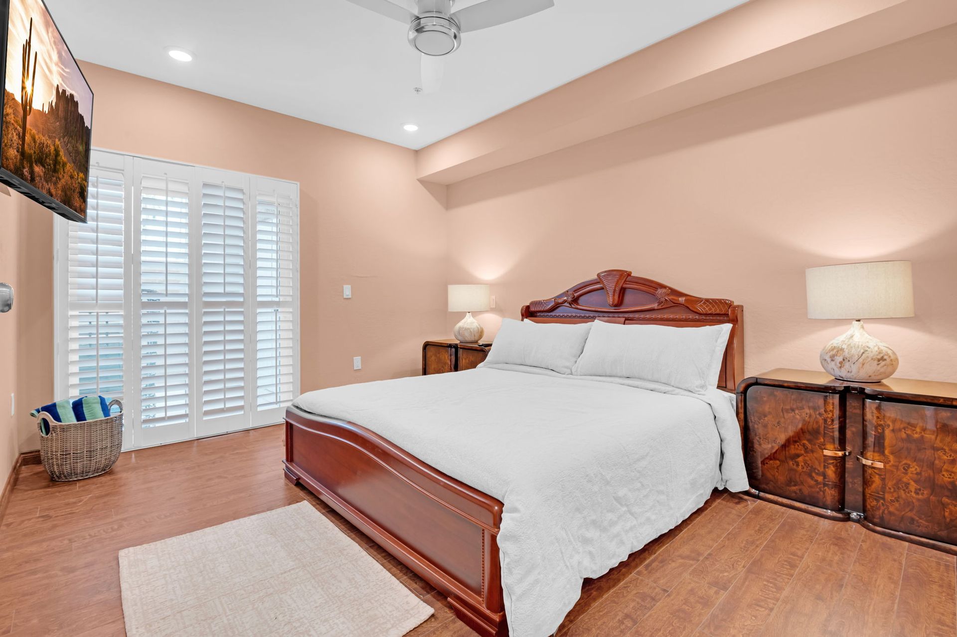 Bedroom with bed, nightstands, shutters, and TV; peach walls, brown floor.