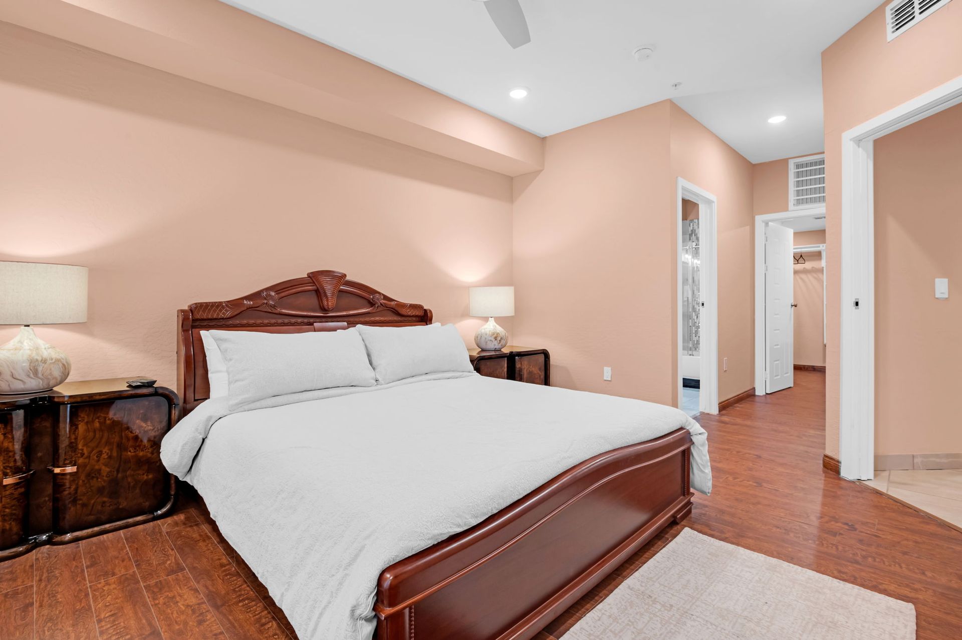 Bedroom with peach walls, wooden floors, a large bed, and access to a walk-in closet.