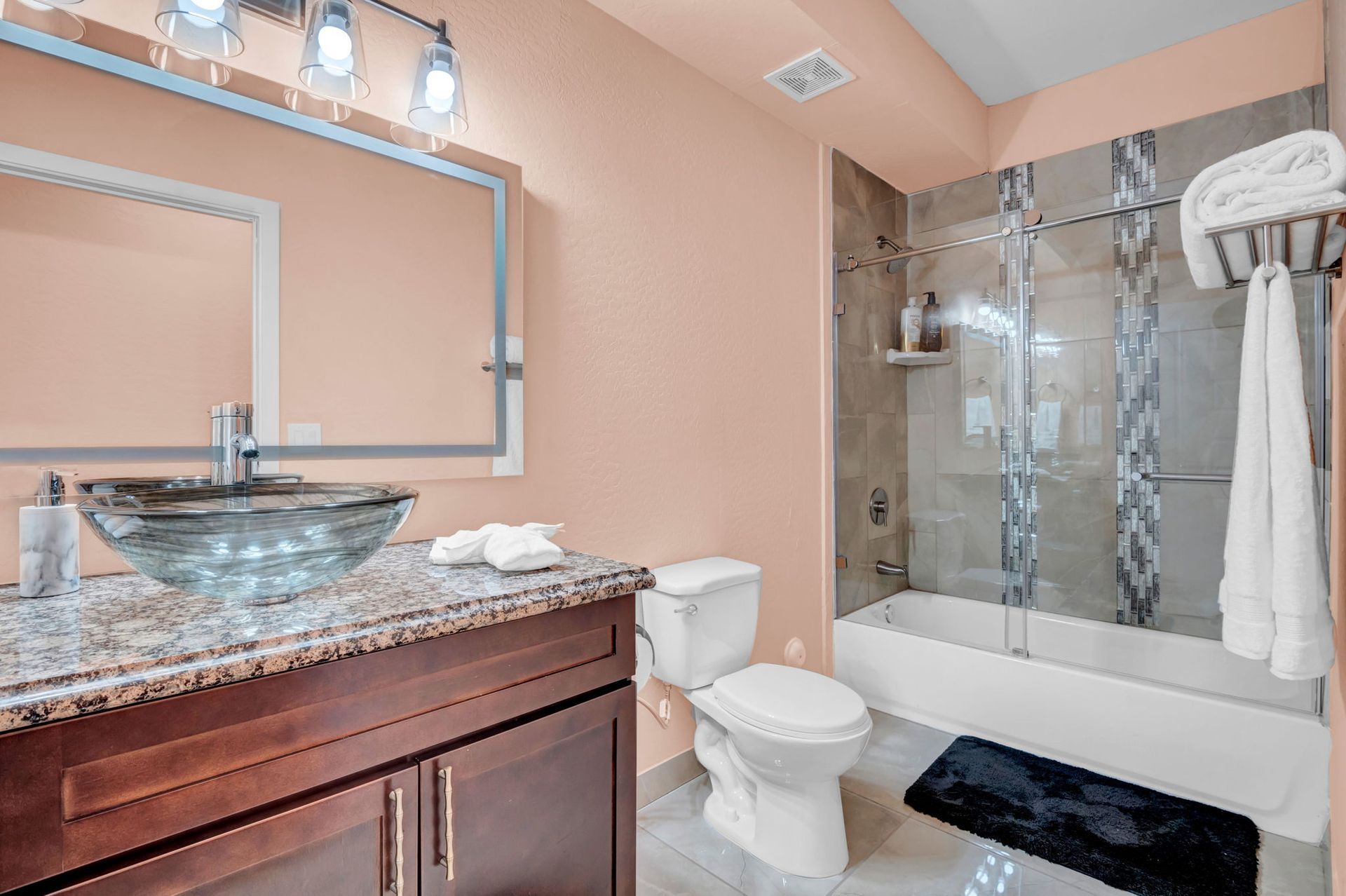 Bathroom with a glass bowl sink on granite countertop, toilet, and shower with glass doors.