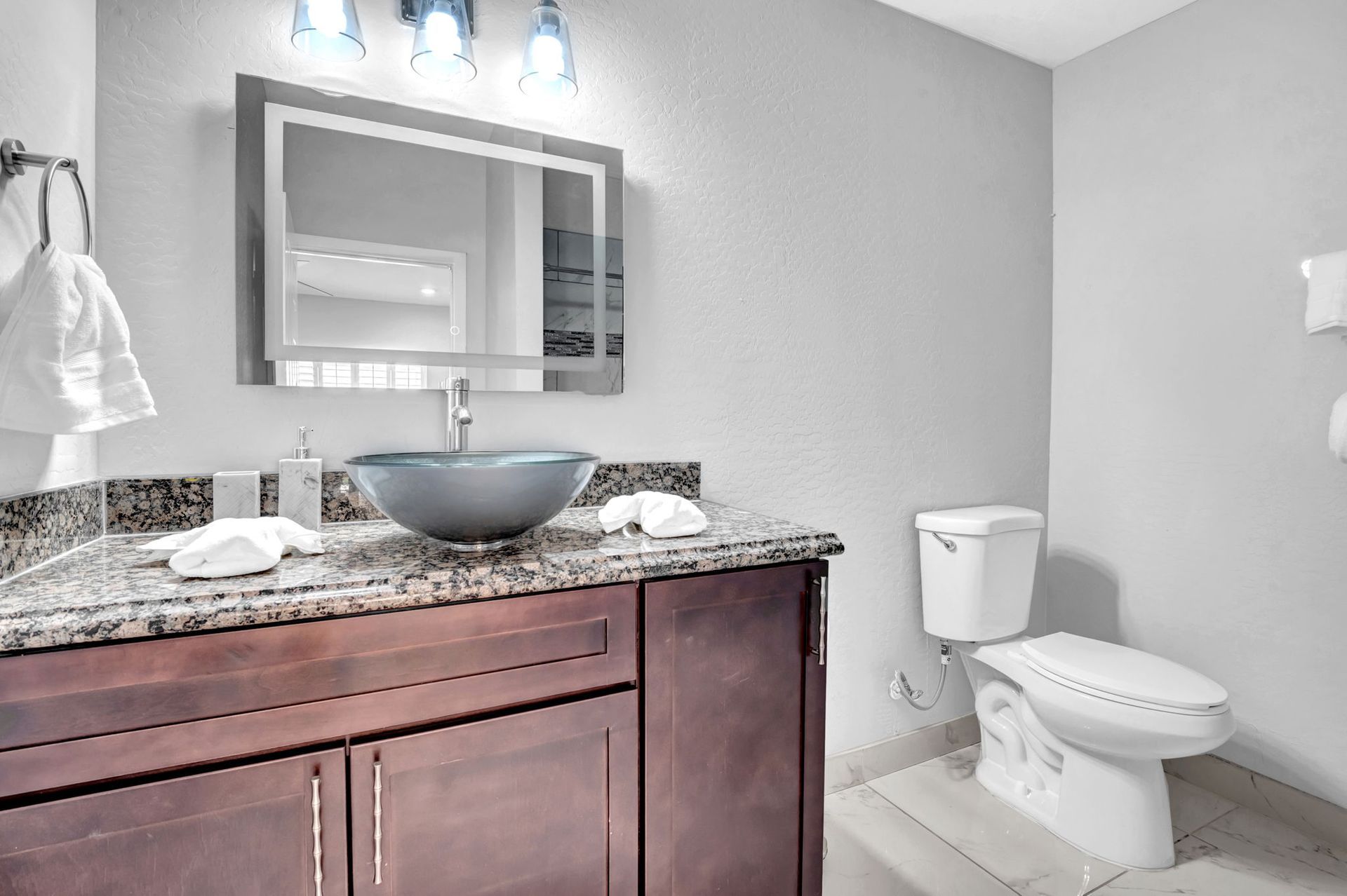 Bathroom with dark wood vanity, granite countertop, vessel sink, toilet, and gray walls.