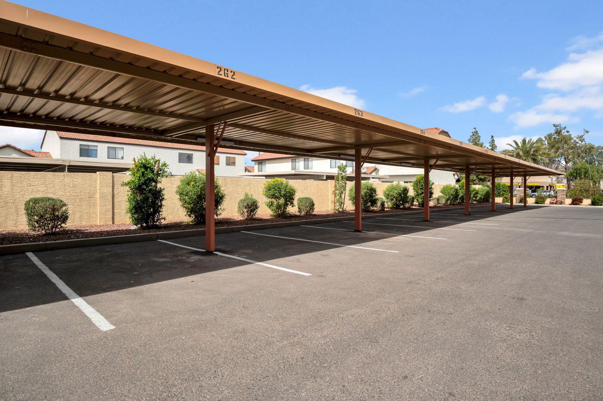 Carport with parking spaces, brown metal roof, brown poles, and asphalt surface.