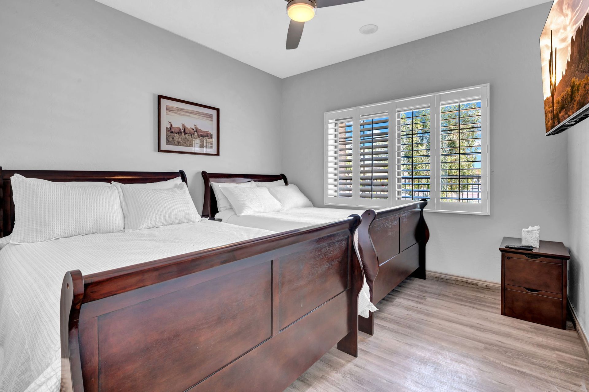 Bedroom with two dark wooden beds, white bedding, and a window with white shutters.