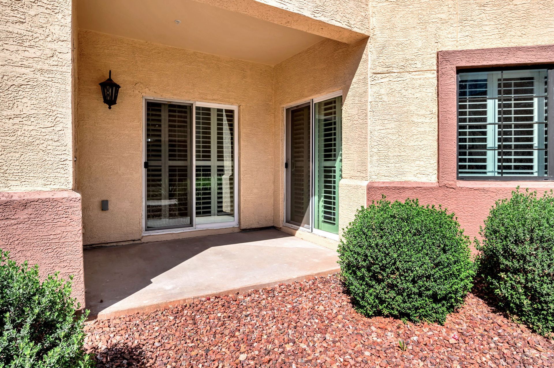 Covered patio with sliding glass doors and shuttered window; green bushes in foreground.
