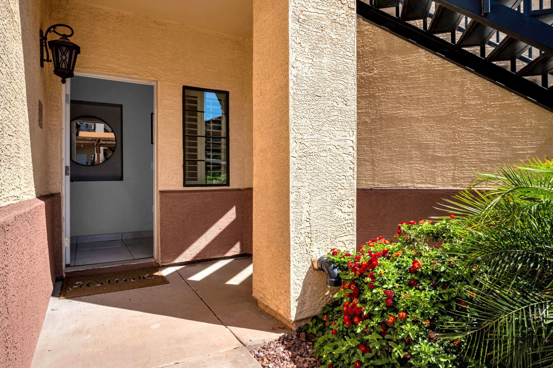 Exterior entrance to a building. Open doorway with a round mirror, window and small red flowering plants.