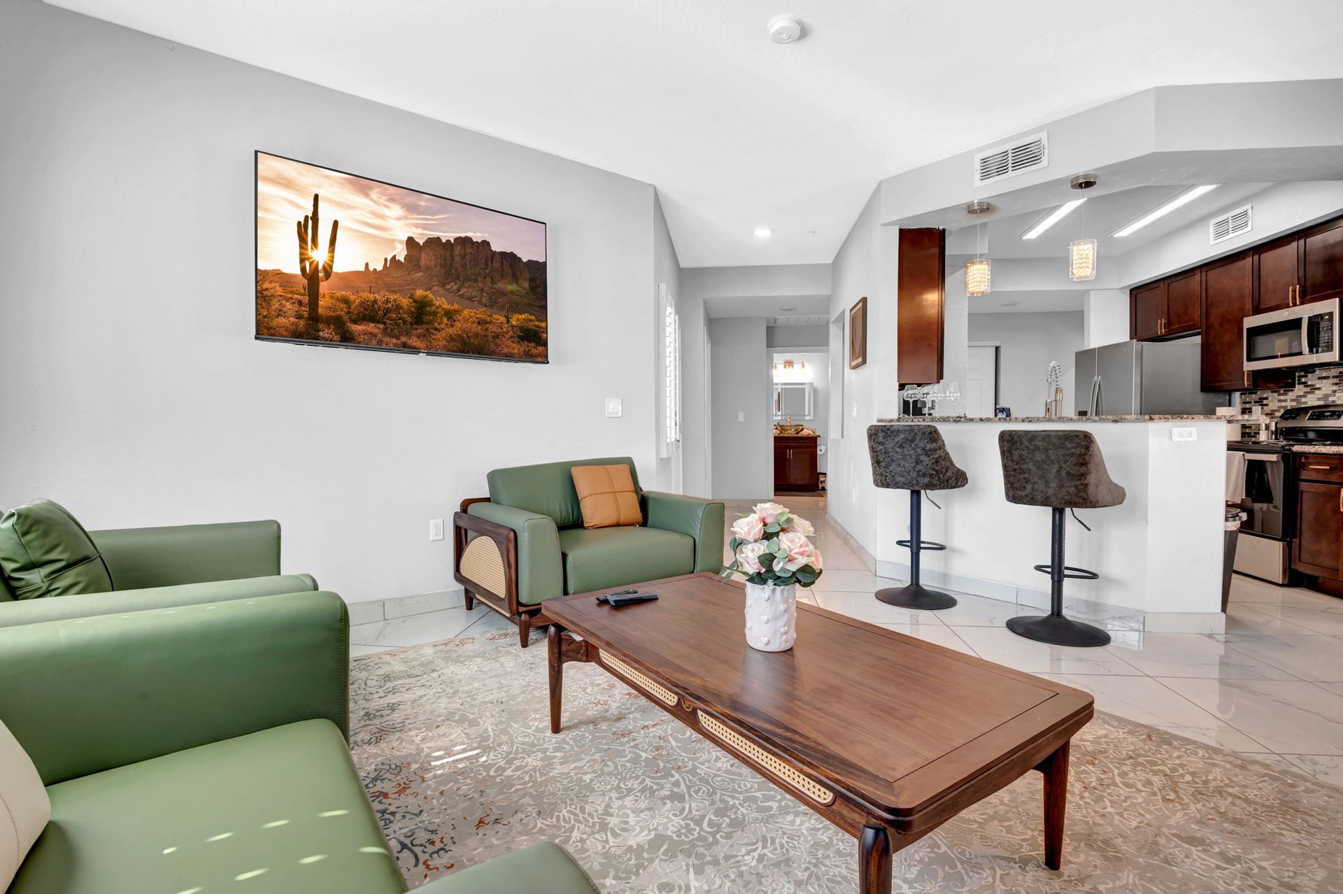 Living room with green couches, wooden coffee table, and kitchen in the background. Southwestern art.