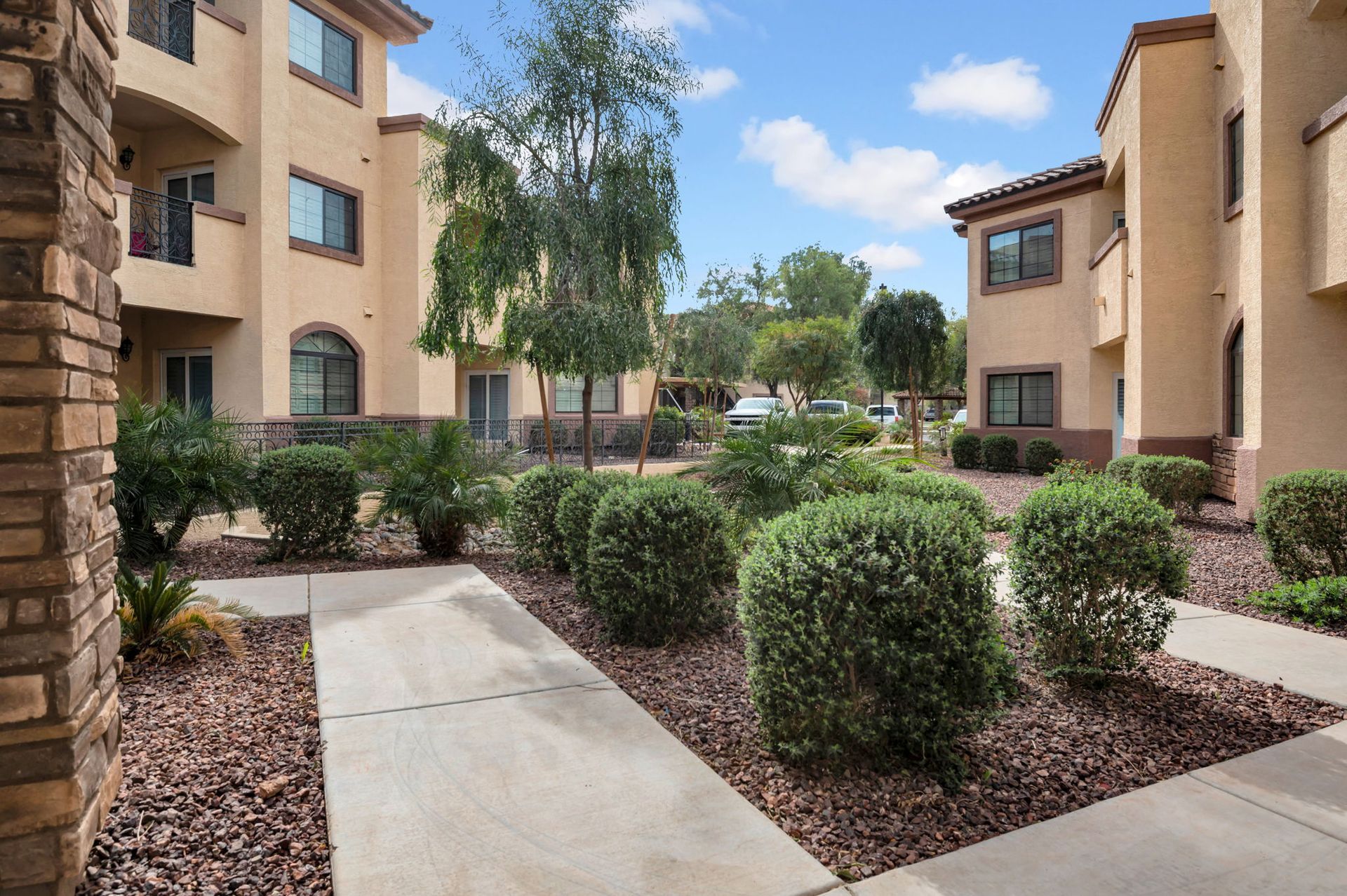 Courtyard with walkways, shrubs, trees, and tan buildings in the background.