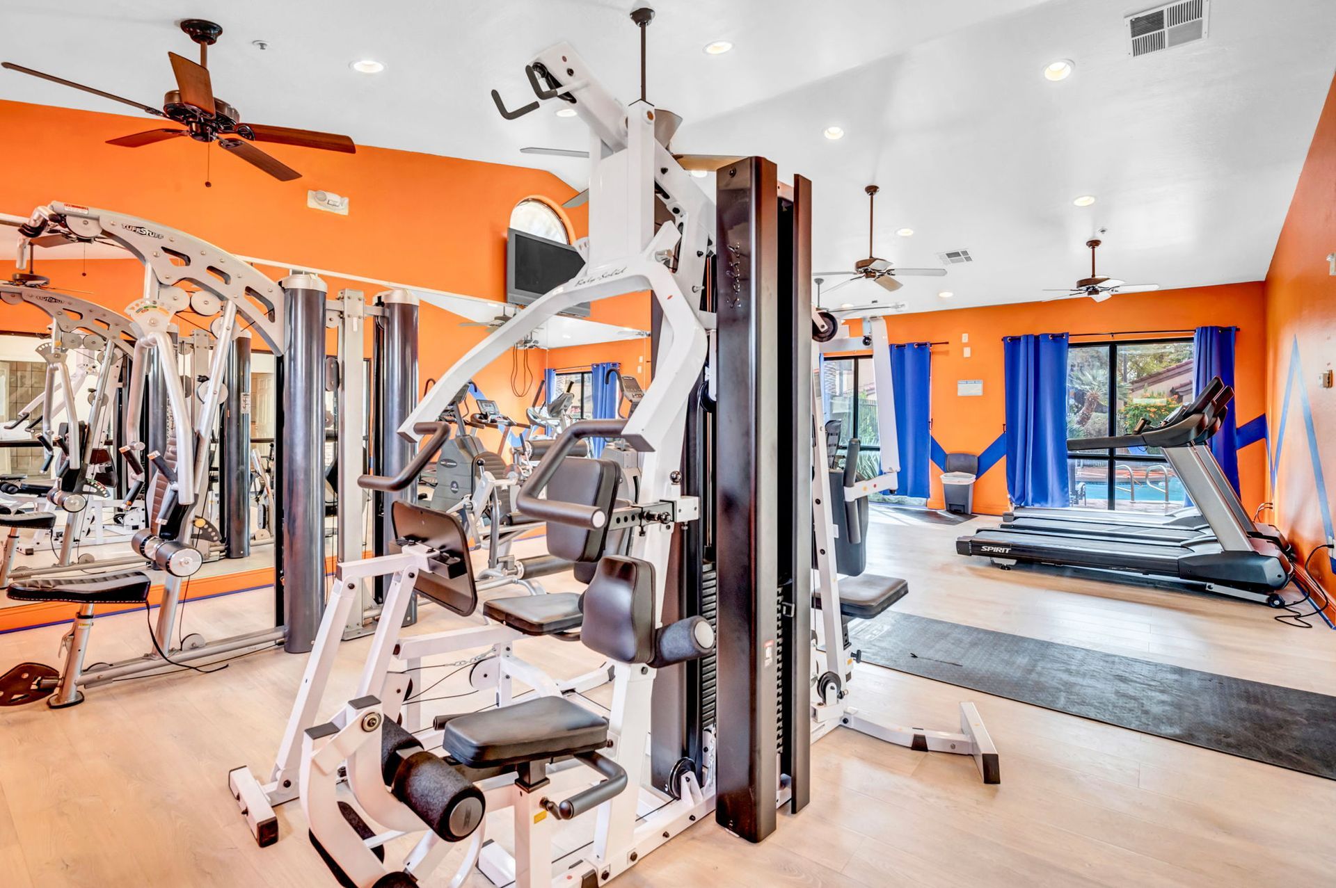 Gym with weight machines, treadmills, and orange walls.