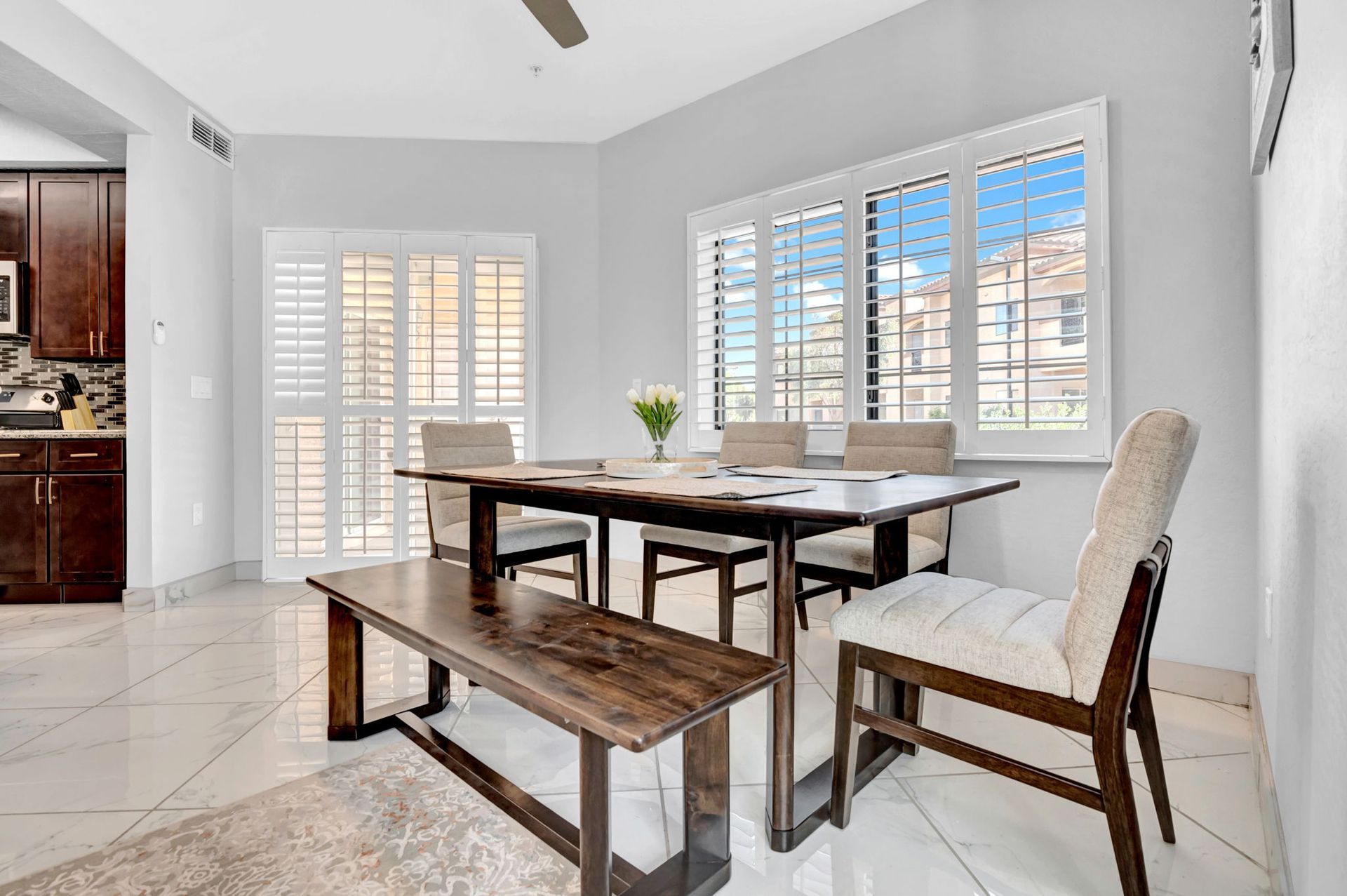 Dining room with table, bench, and chairs, shutters, and window with outdoor view.