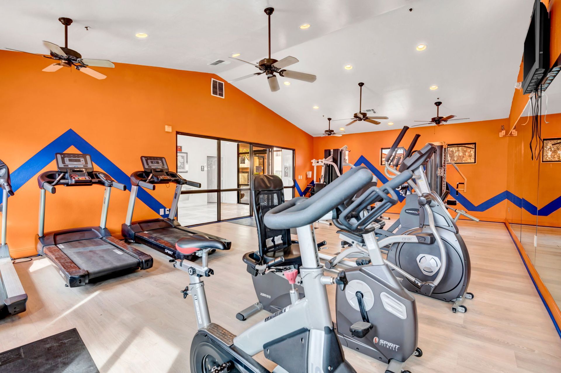 Gym interior with treadmills, stationary bikes, and other exercise equipment; orange walls.