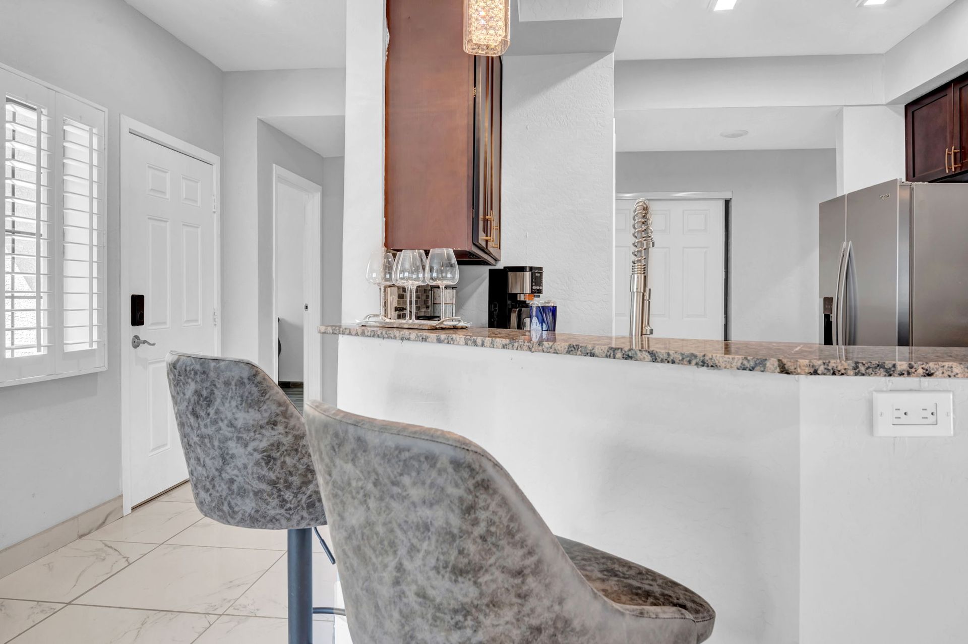 Kitchen with gray bar stools, countertop, cabinets, and stainless steel appliances.