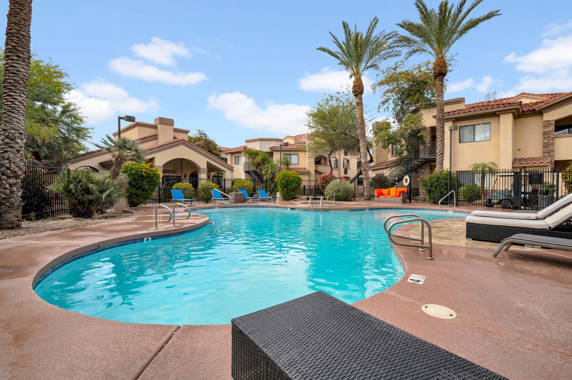Pool in front of a multi-story apartment complex with palm trees under a blue sky.