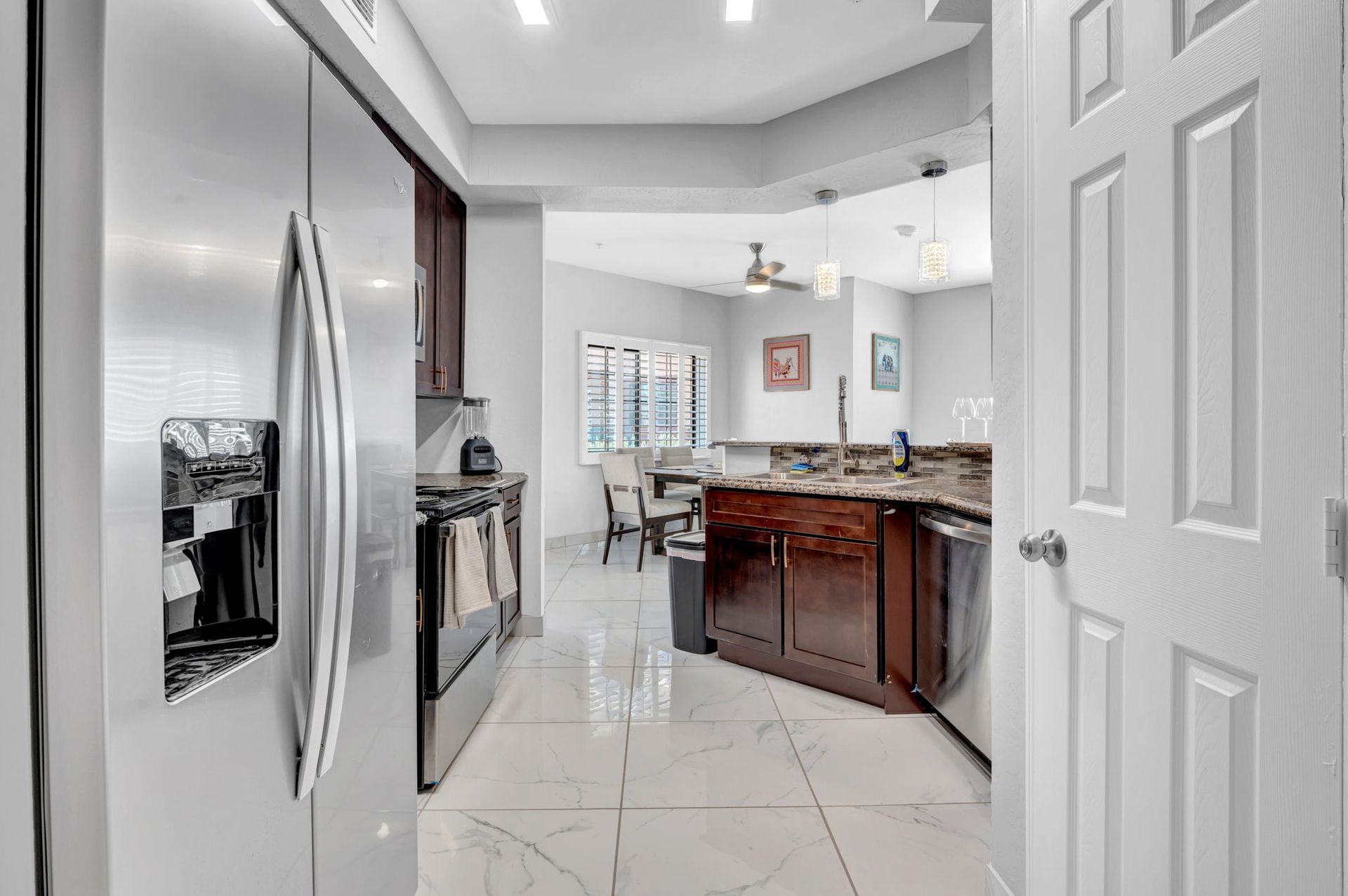 Kitchen with stainless steel appliances, dark wood cabinets, and tile floor, leading to a dining area.