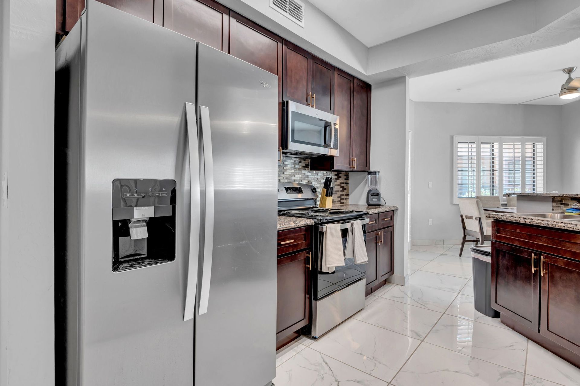 Stainless steel refrigerator and dark wood cabinetry in a kitchen with marble flooring.