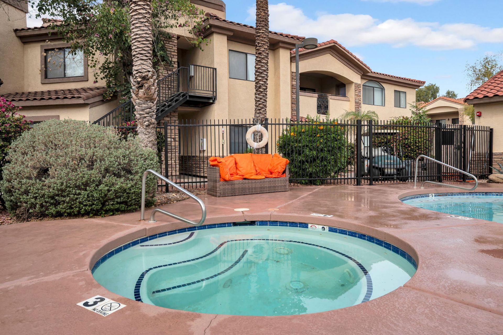 Hot tub and pool area in front of an apartment building with outdoor seating and palm trees.