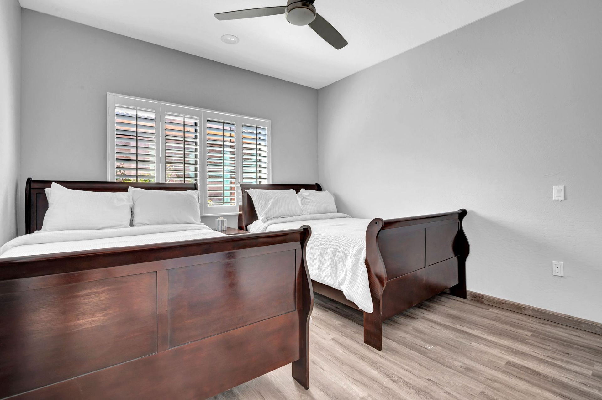 Bedroom with two dark wooden twin beds, a window with shutters, and a ceiling fan.