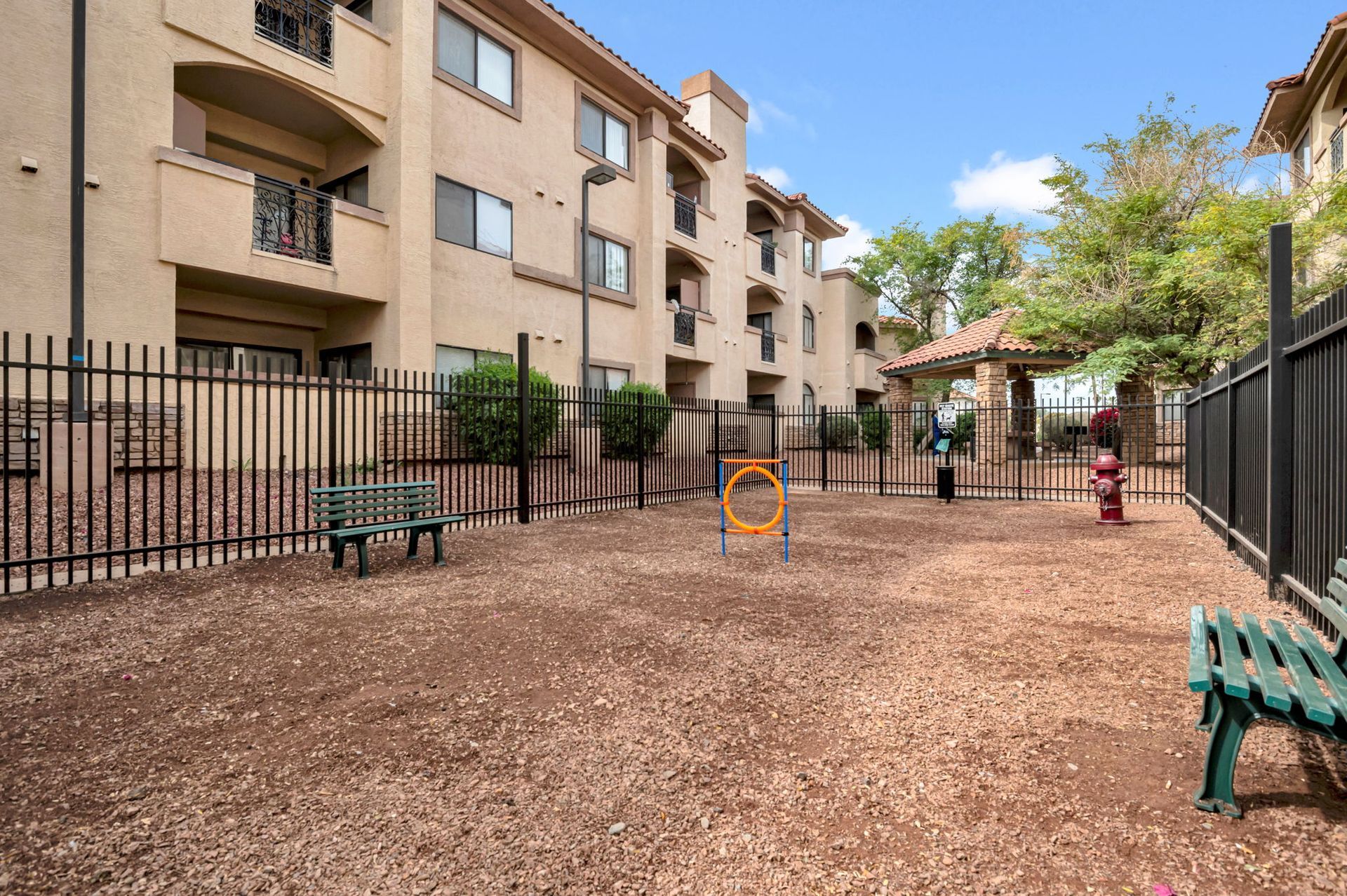 Dog park at an apartment complex with benches, agility equipment, and a gazebo, surrounded by a black fence.
