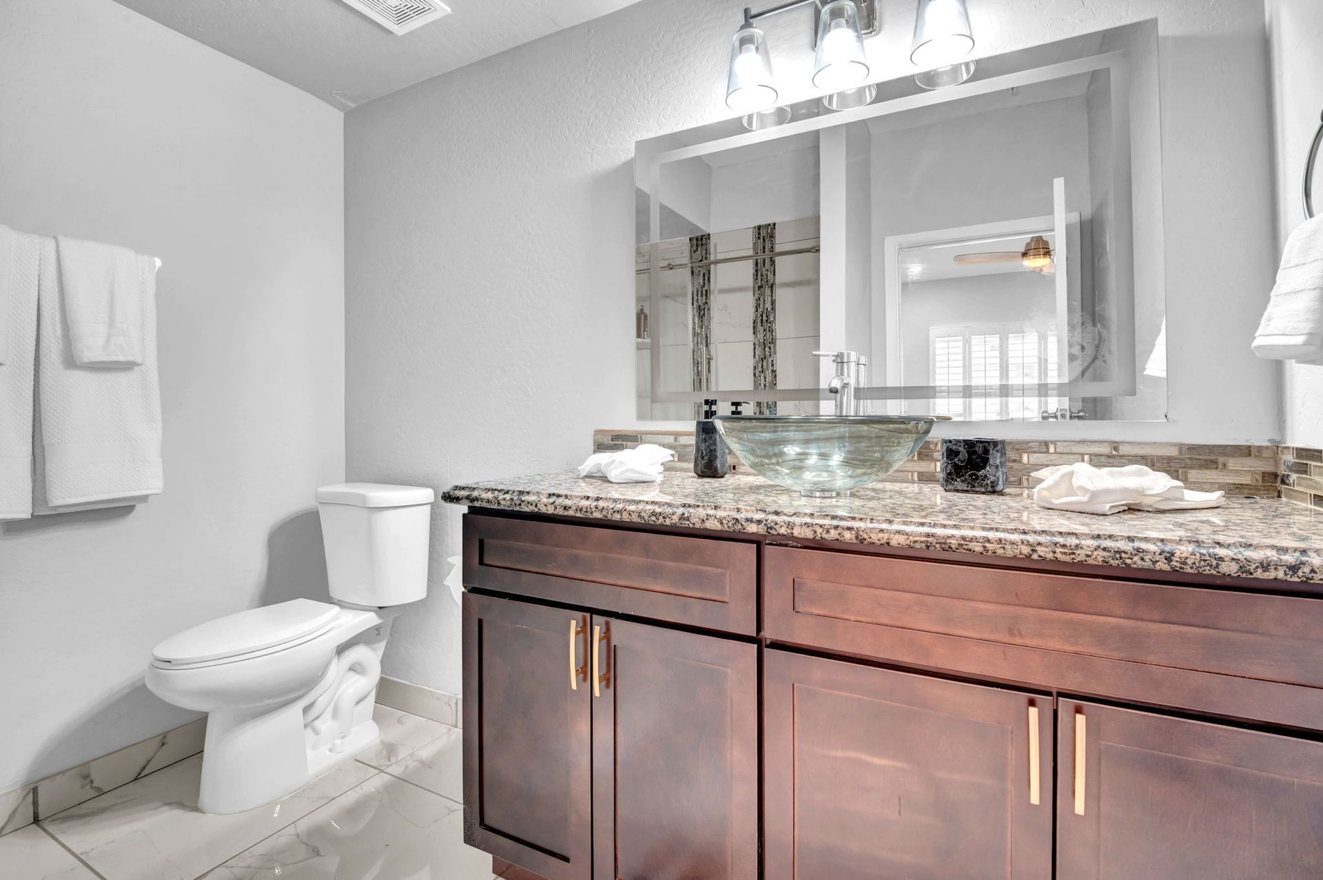 Bathroom with dark wood vanity, glass bowl sink, large mirror, and white towels.