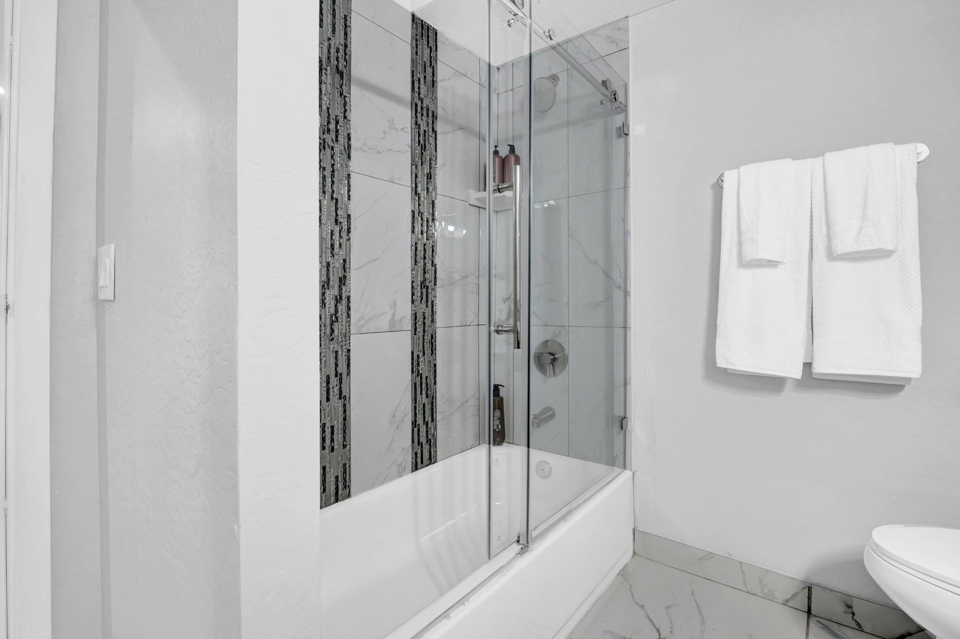 Bathroom with glass shower door, white and gray tiles, and two white towels.