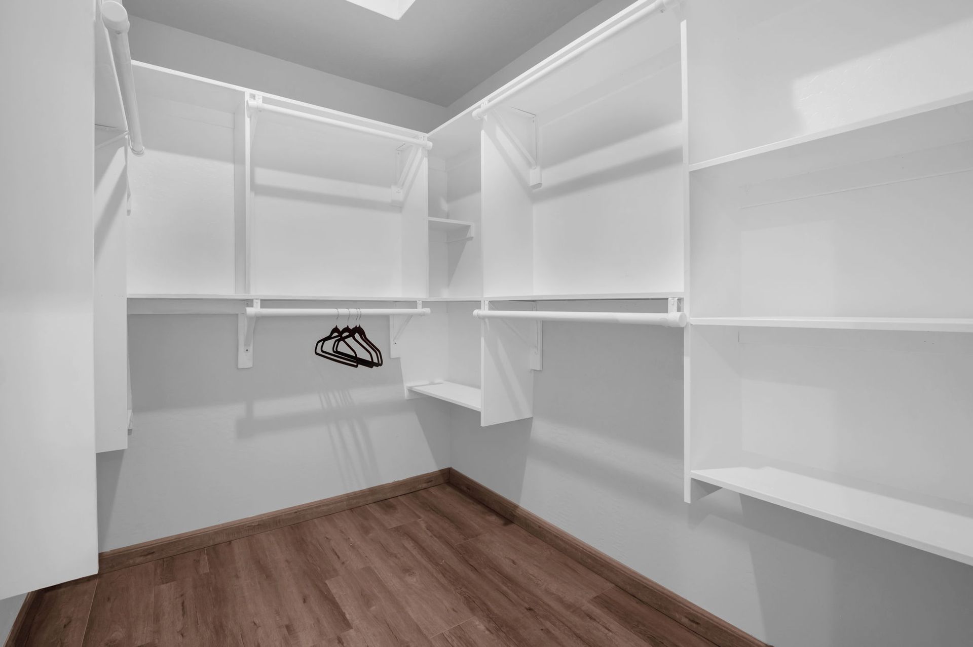 Empty walk-in closet with white shelves and rods. Dark wood floor.