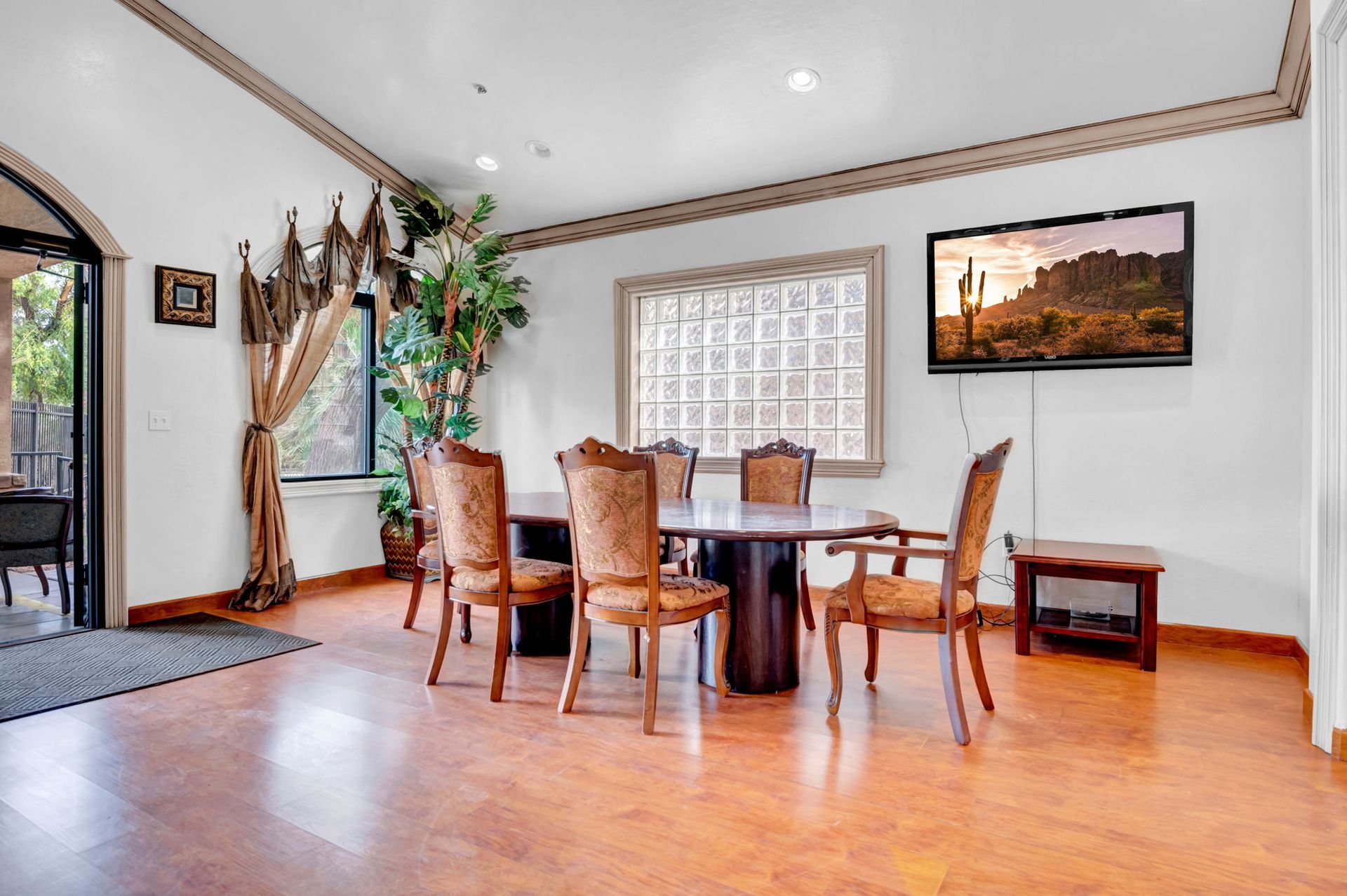 Dining room with wooden table, chairs, and TV; window with curtains; wood flooring.
