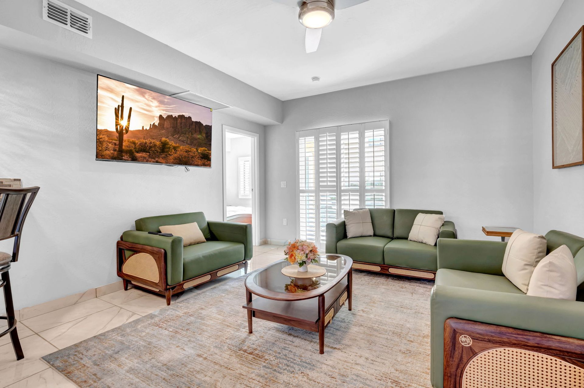 Living room with green sofas, a coffee table, a rug, and a TV showing a desert landscape.
