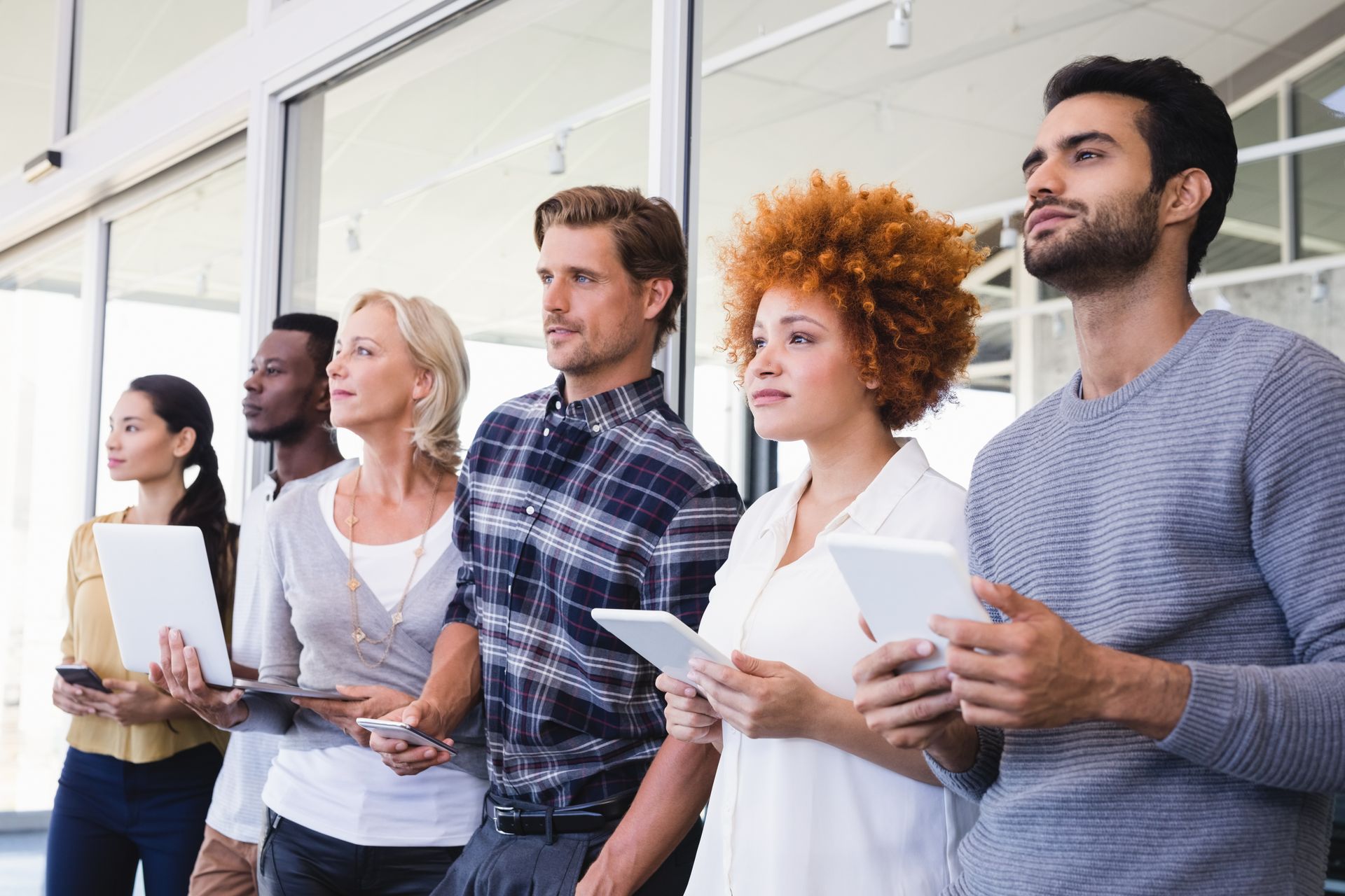 Group of people are standing in a row holding tablets and computers.