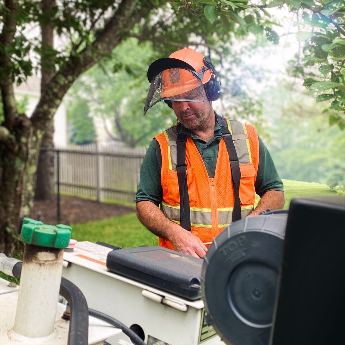 A man wearing an orange vest and helmet is working on a machine.