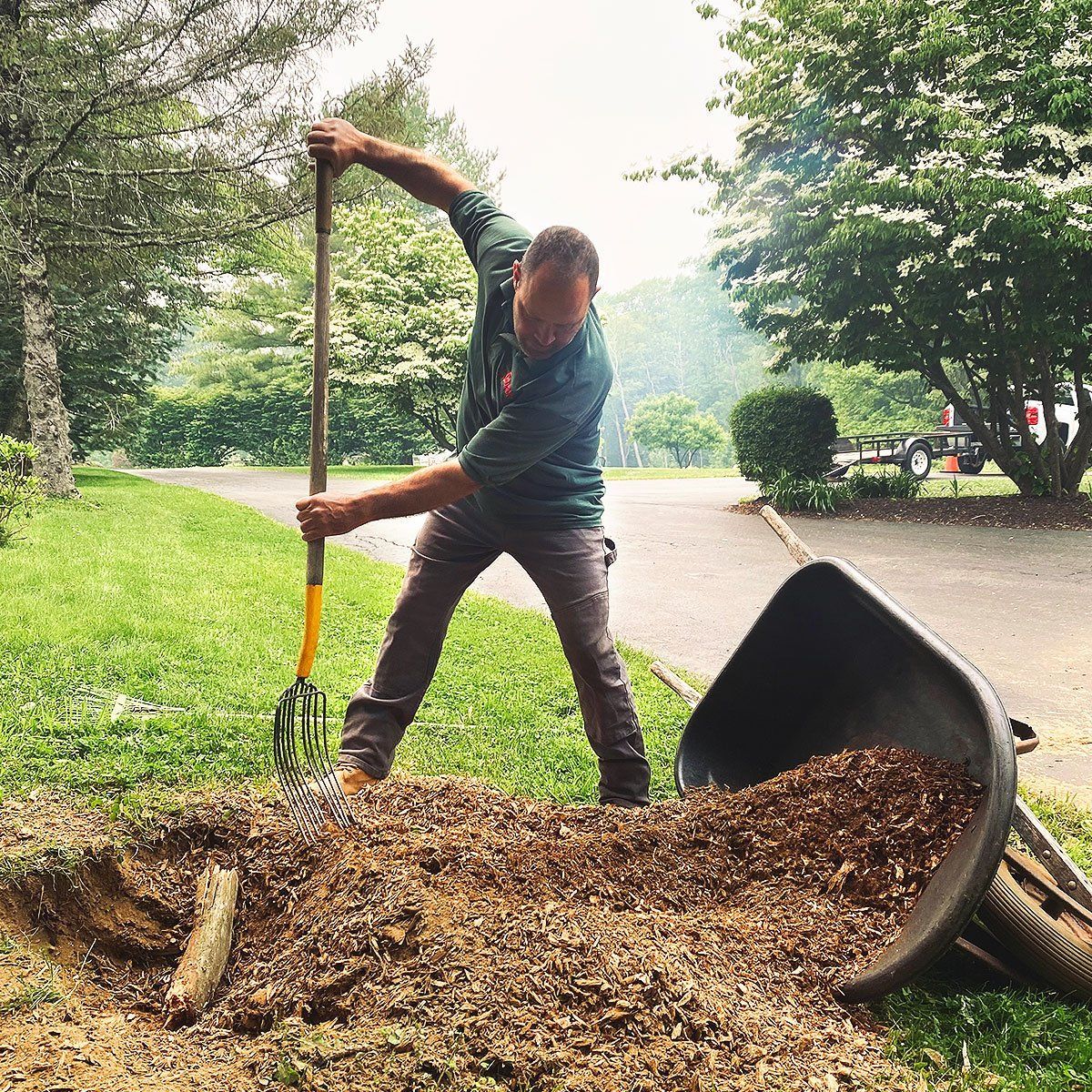 A man is holding a rake over a pile of mulch.