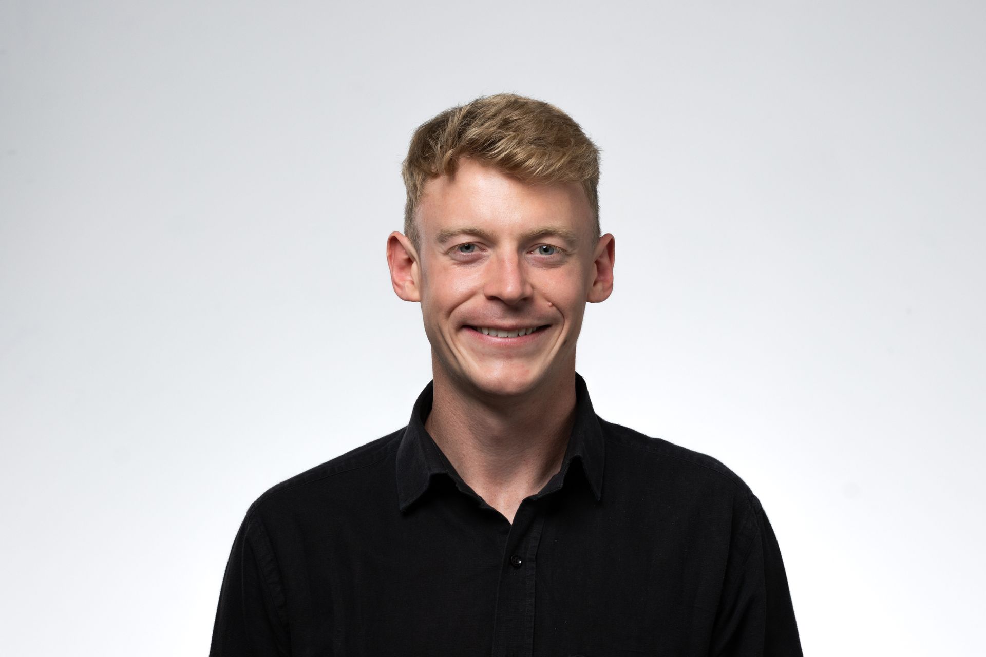 Smiling person with blonde hair wearing a black button-up shirt against a white background.