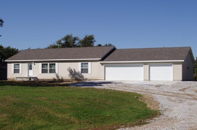 A house with two garage doors is surrounded by grass and gravel