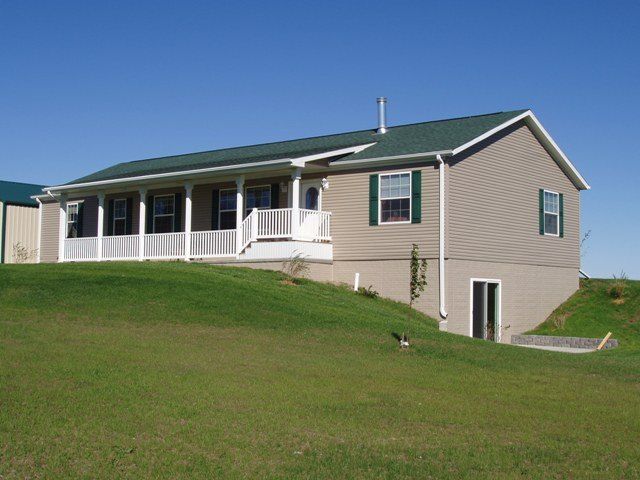 A house with a green roof sits on top of a grassy hill