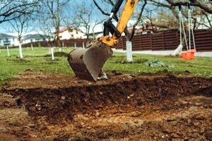 A bulldozer is digging a hole in the ground in a yard.