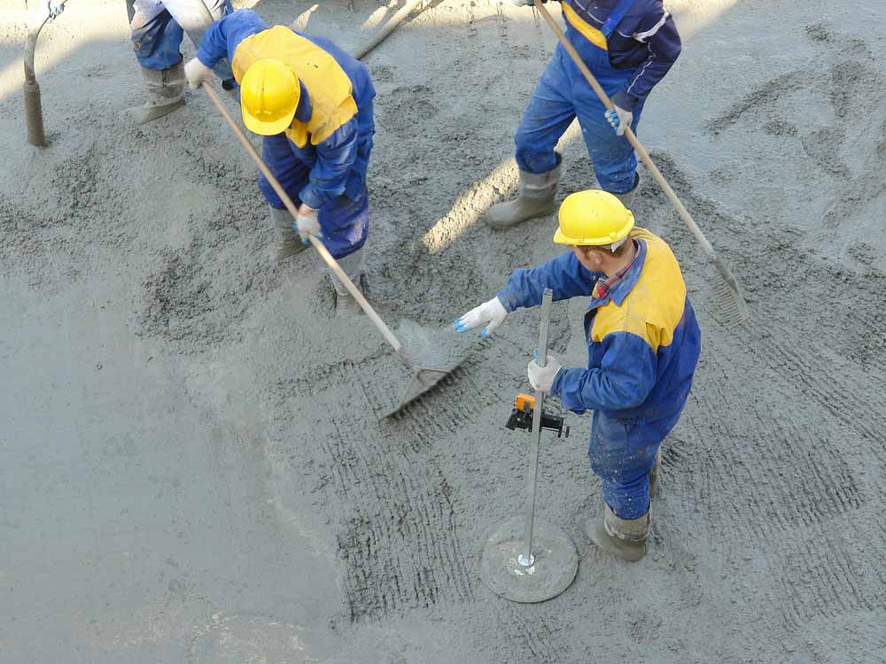 Construction Workers Spreading Freshly Poured Concrete Mix at The Building Site — Easy Mix Concrete in Berkeley Vale, NSW