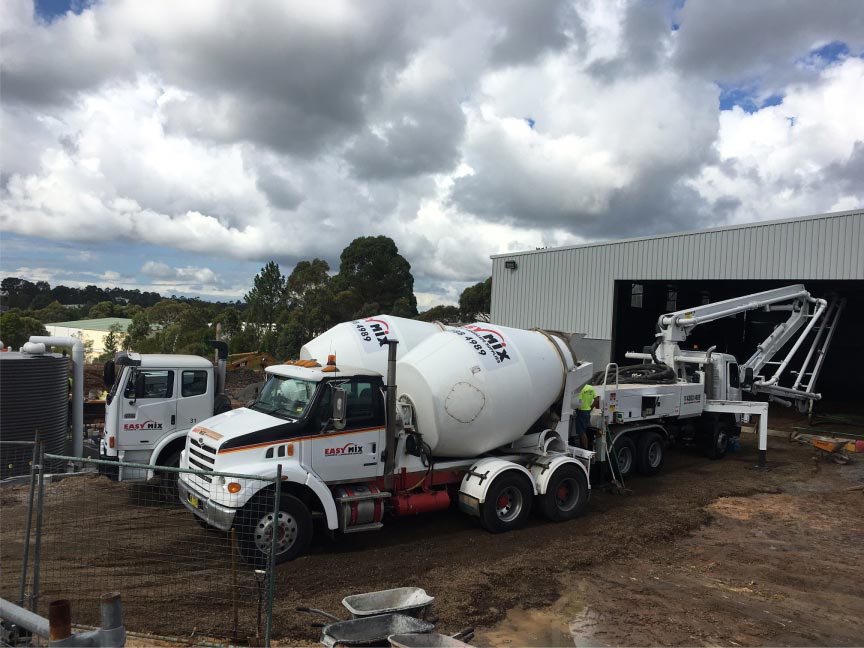 Easy Mix Concrete trucks delivering concrete at a commercial construction site with workers and mach