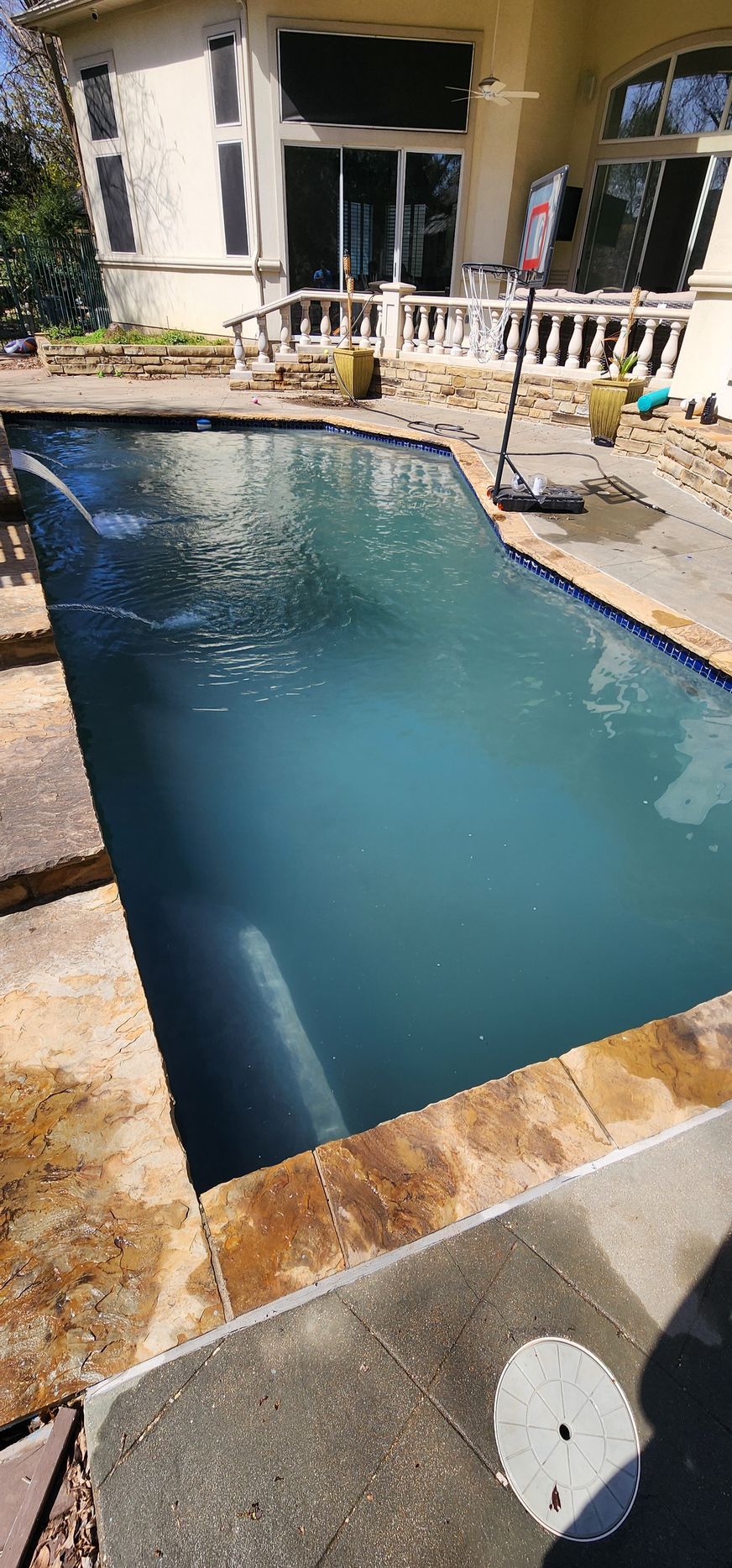 Swimming pool in a backyard, with a house in the background. The water is a light blue color.