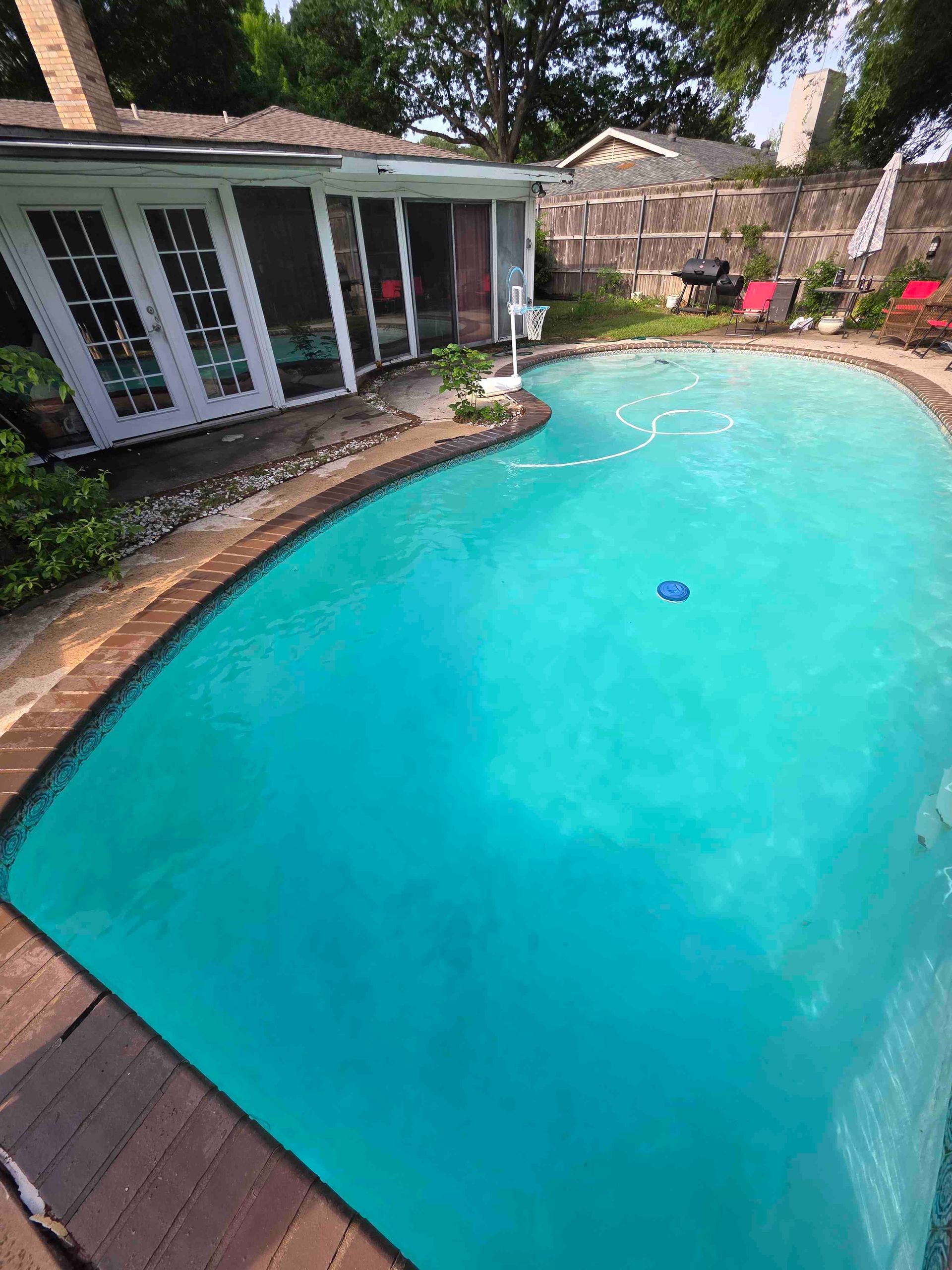 Pool with turquoise water, surrounded by brick patio, near a house with French doors and a screened-in porch.