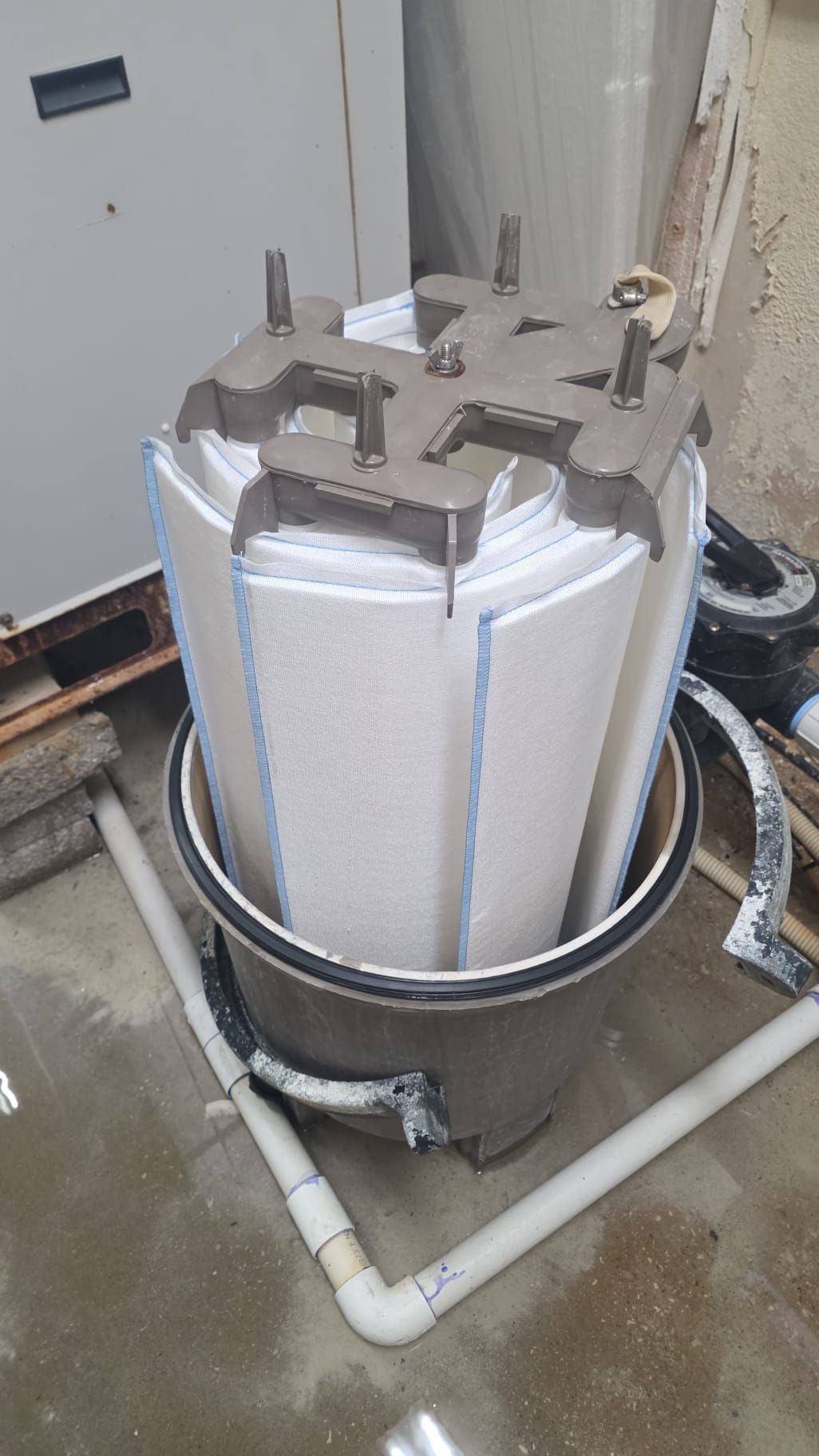 Large white filter cartridge inside a metal container with gray top and white PVC piping.